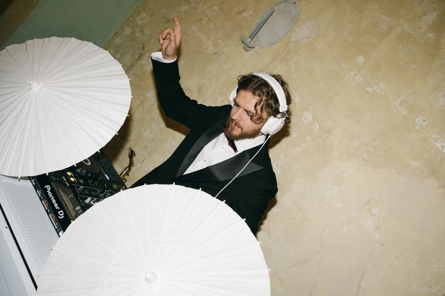 DJ in tuxedo wearing white headphones mixing music at a wedding reception, viewed from above.