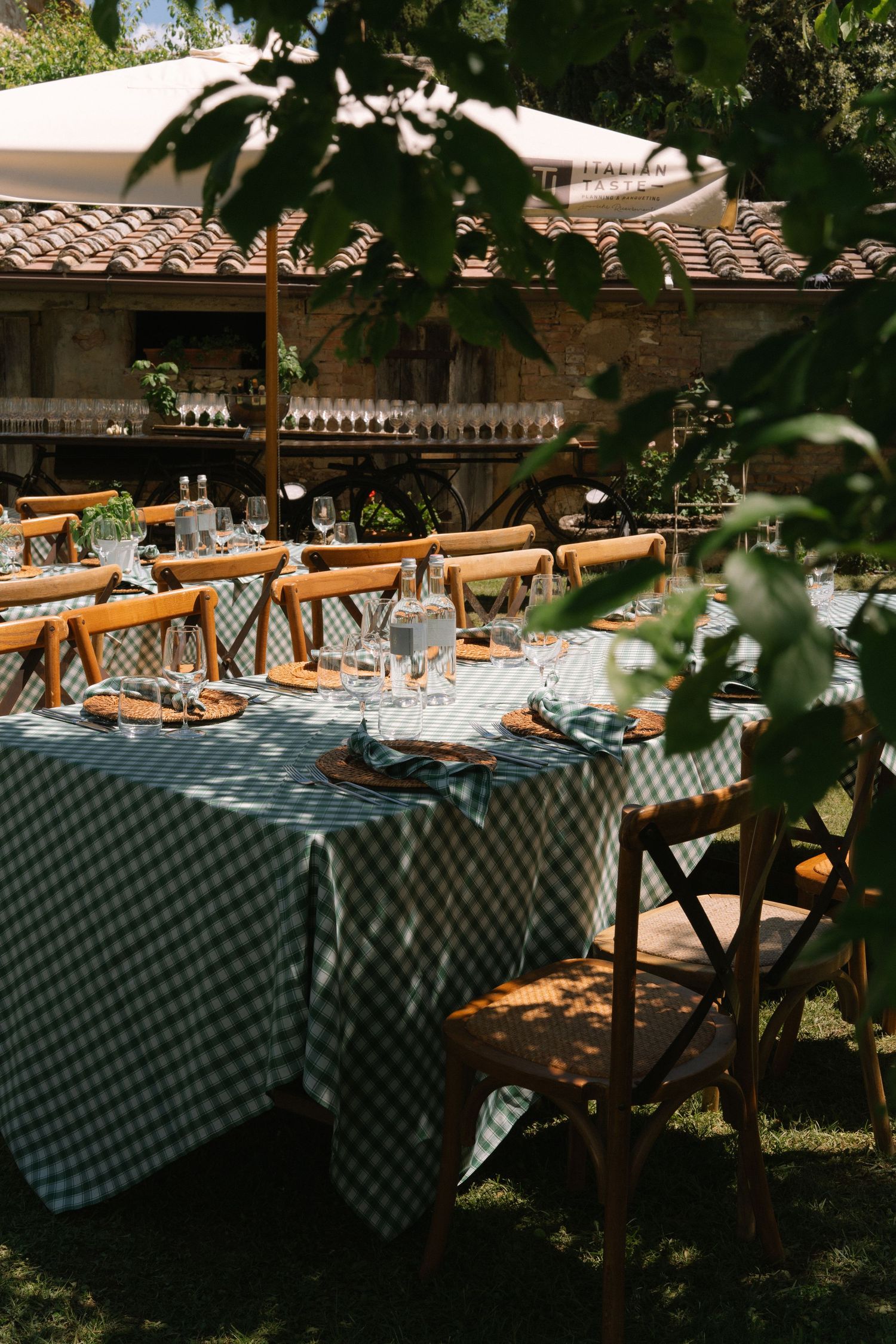 Elegant outdoor dining table set with gingham tablecloth, wooden chairs, and glassware.