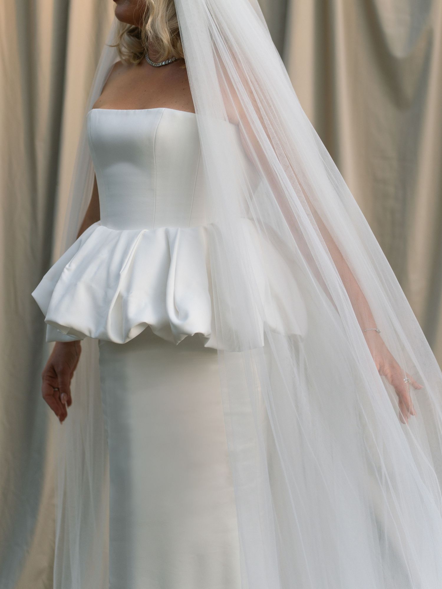 Elegant strapless white satin peplum wedding dress with flowing cathedral veil on blonde bride.