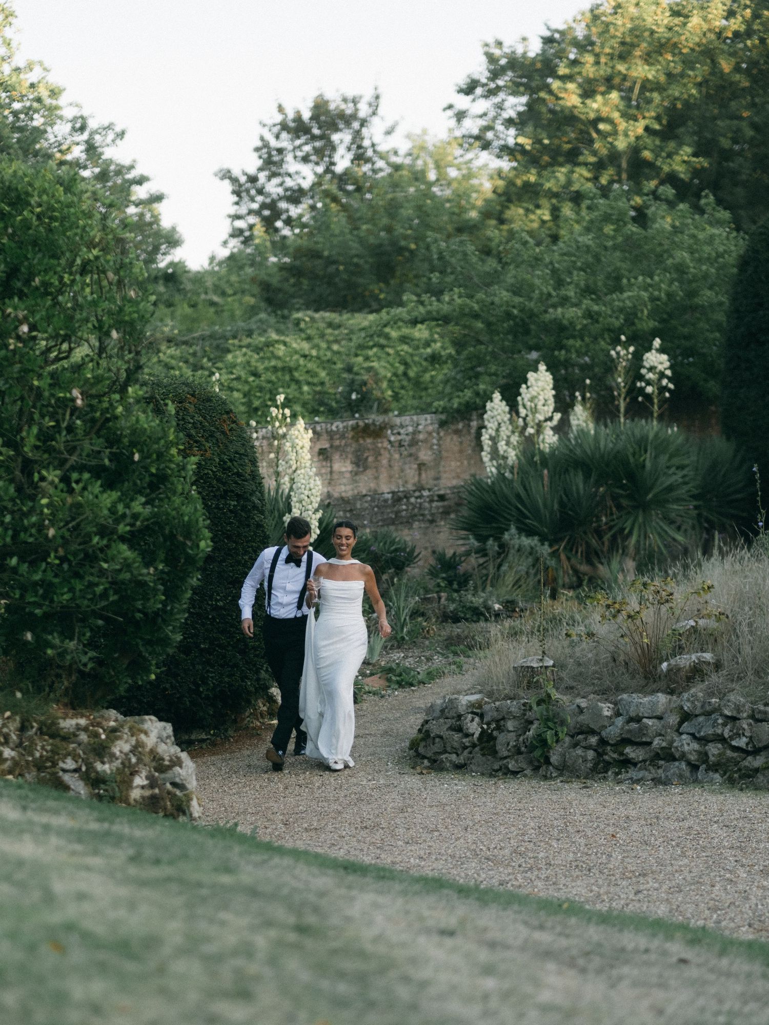 Bride and groom walk hand-in-hand through a lush garden path on their wedding day.