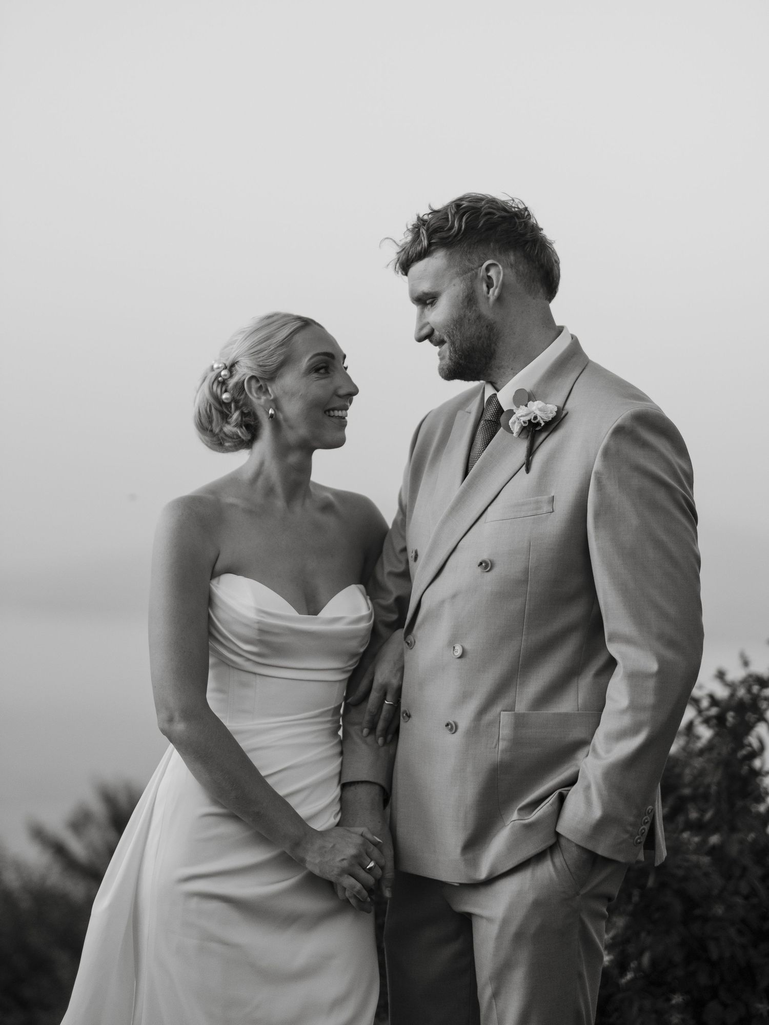Black and white portrait of smiling bride and groom holding hands at outdoor wedding.