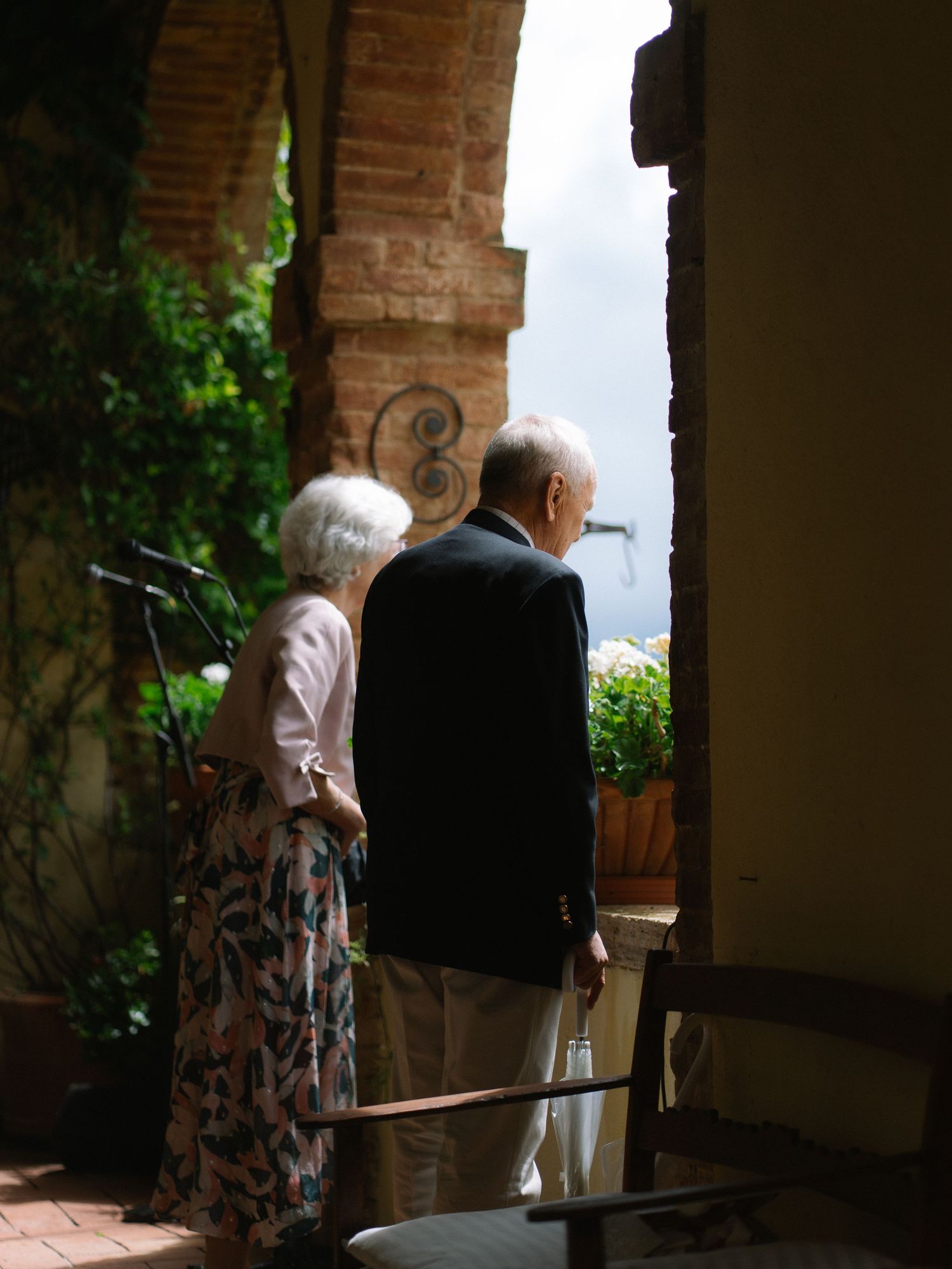 Elderly couple standing together in arched doorway overlooking lush garden at wedding.
