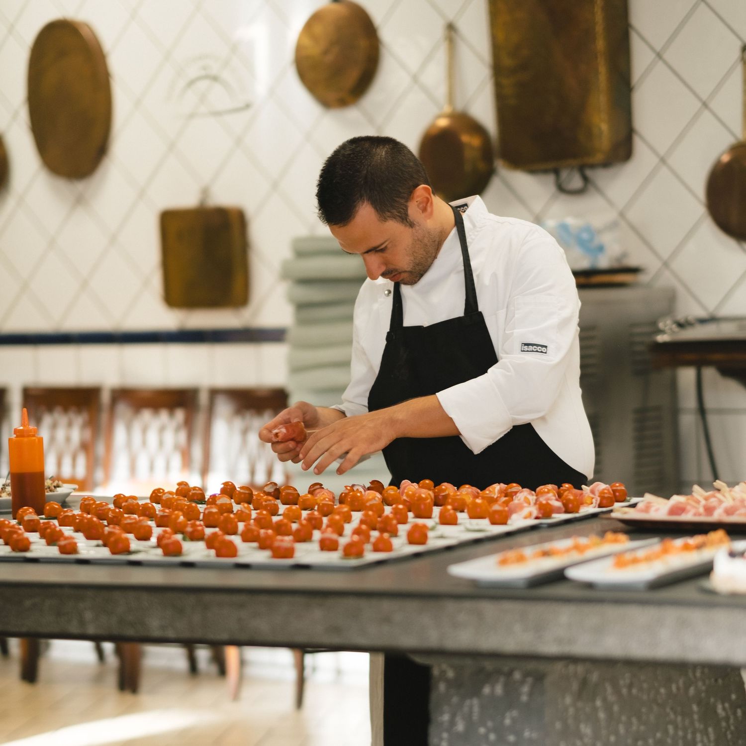 Professional chef in white coat carefully arranges appetizers on trays in an elegant kitchen.