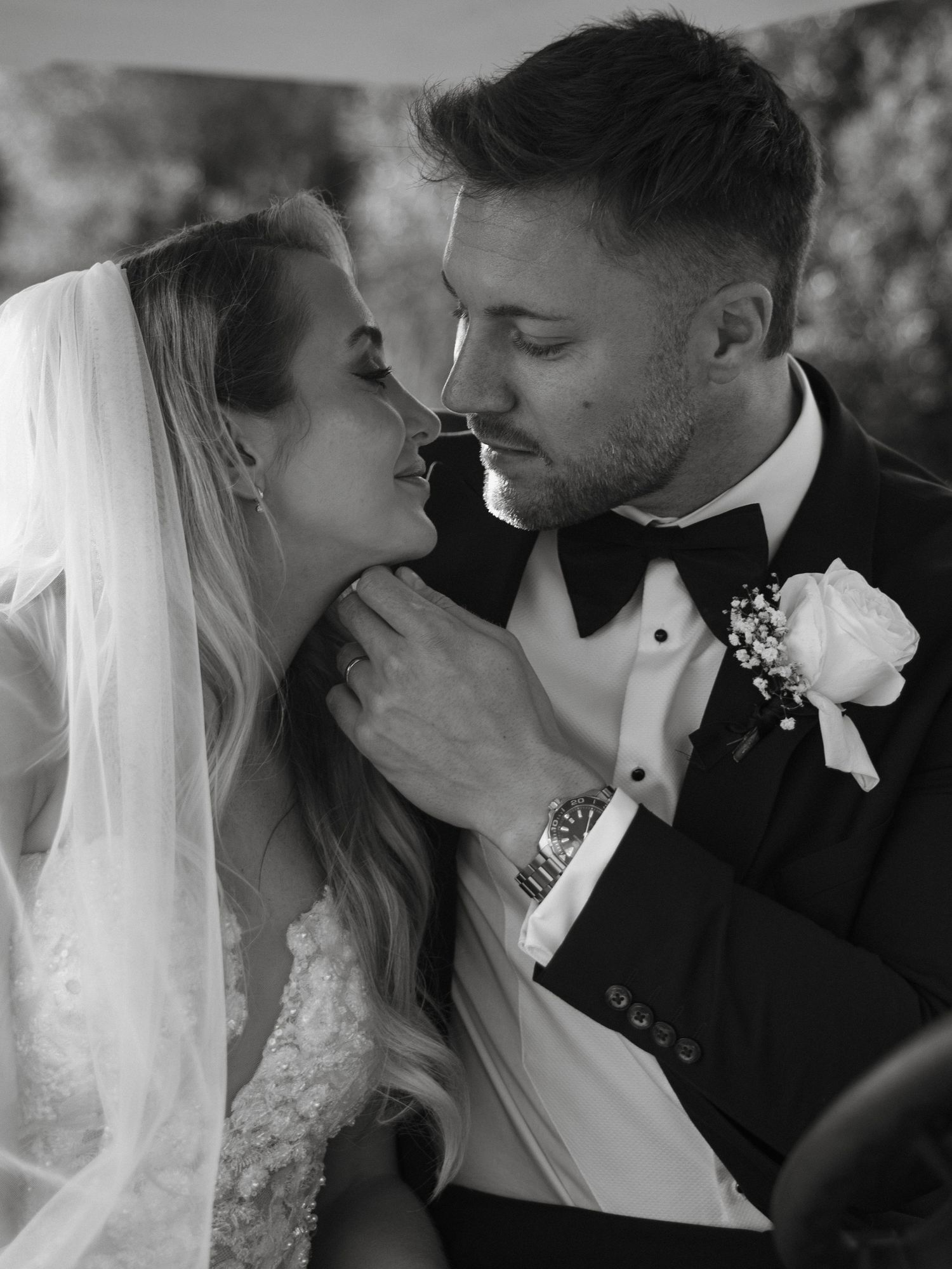 Black and white wedding photo of bride in veil and groom in tuxedo sharing an intimate moment.