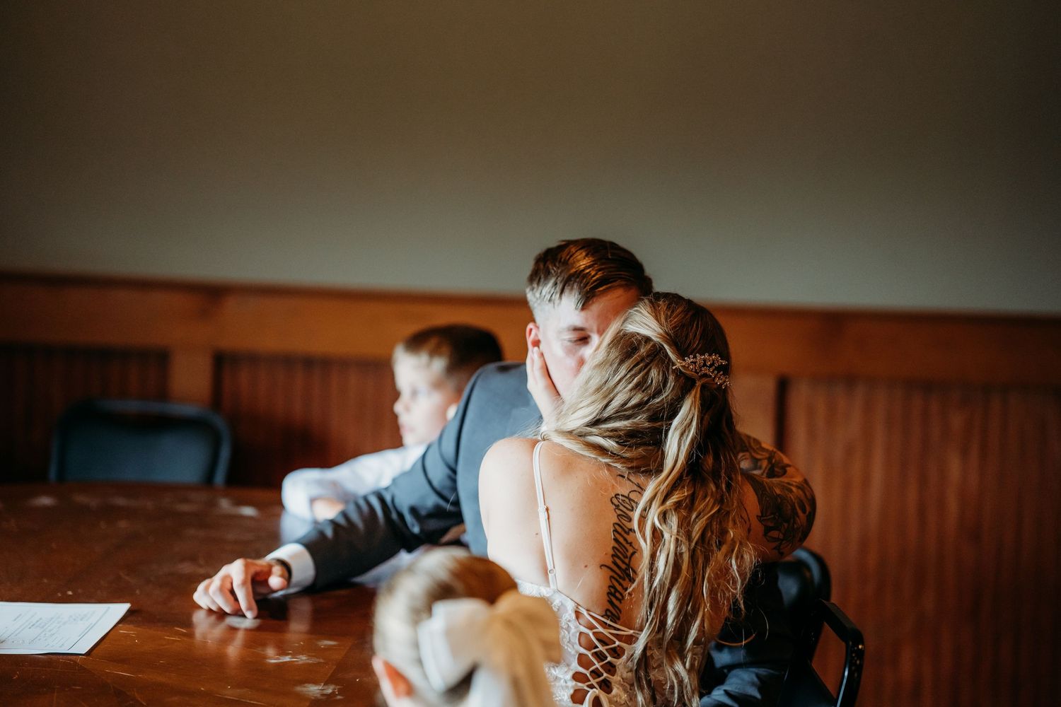 Bride and groom share an intimate moment at a wooden table during wedding ceremony signing.
