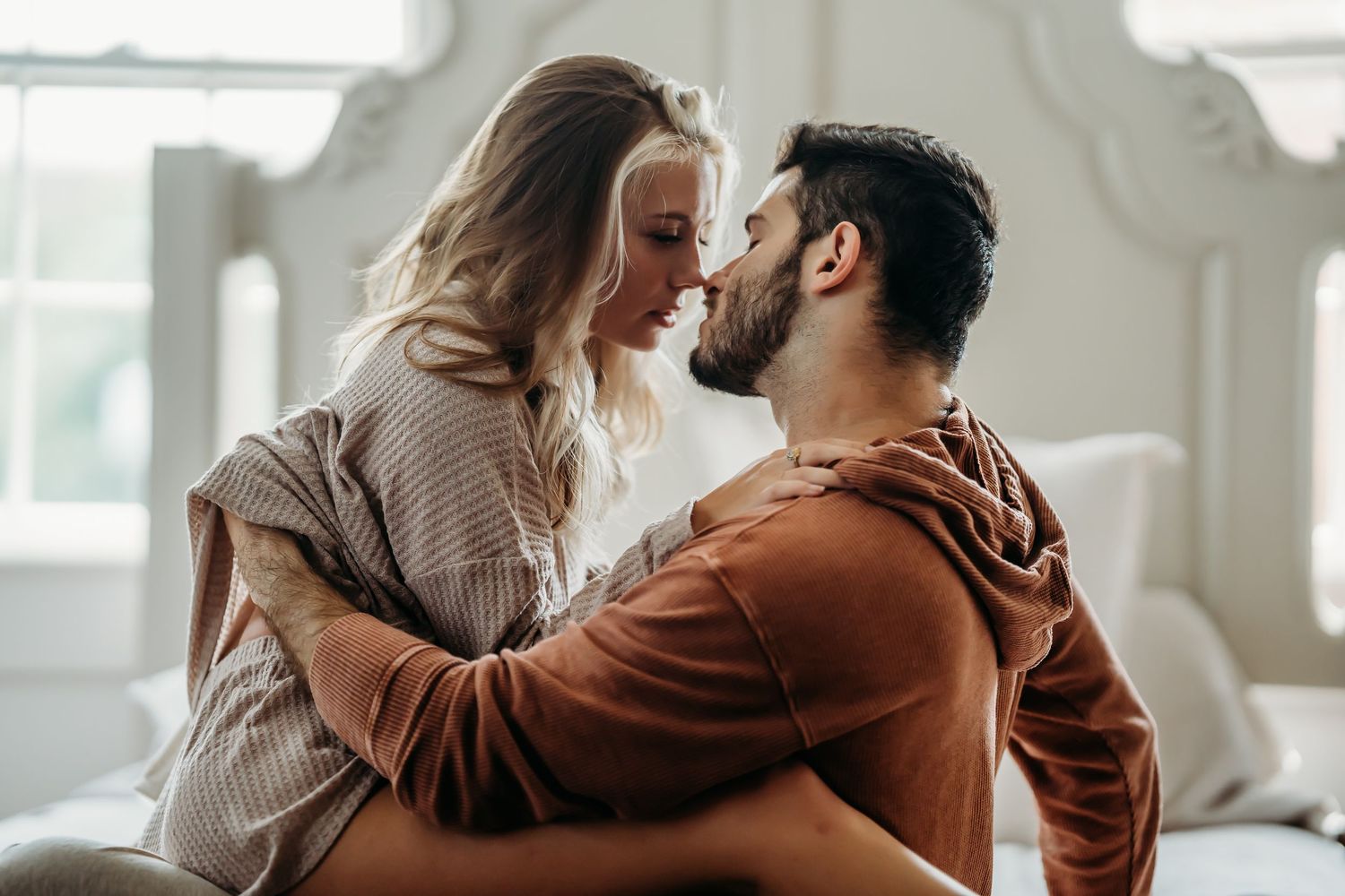 Loving couple leaning in for a kiss while sitting together on a bed indoors.