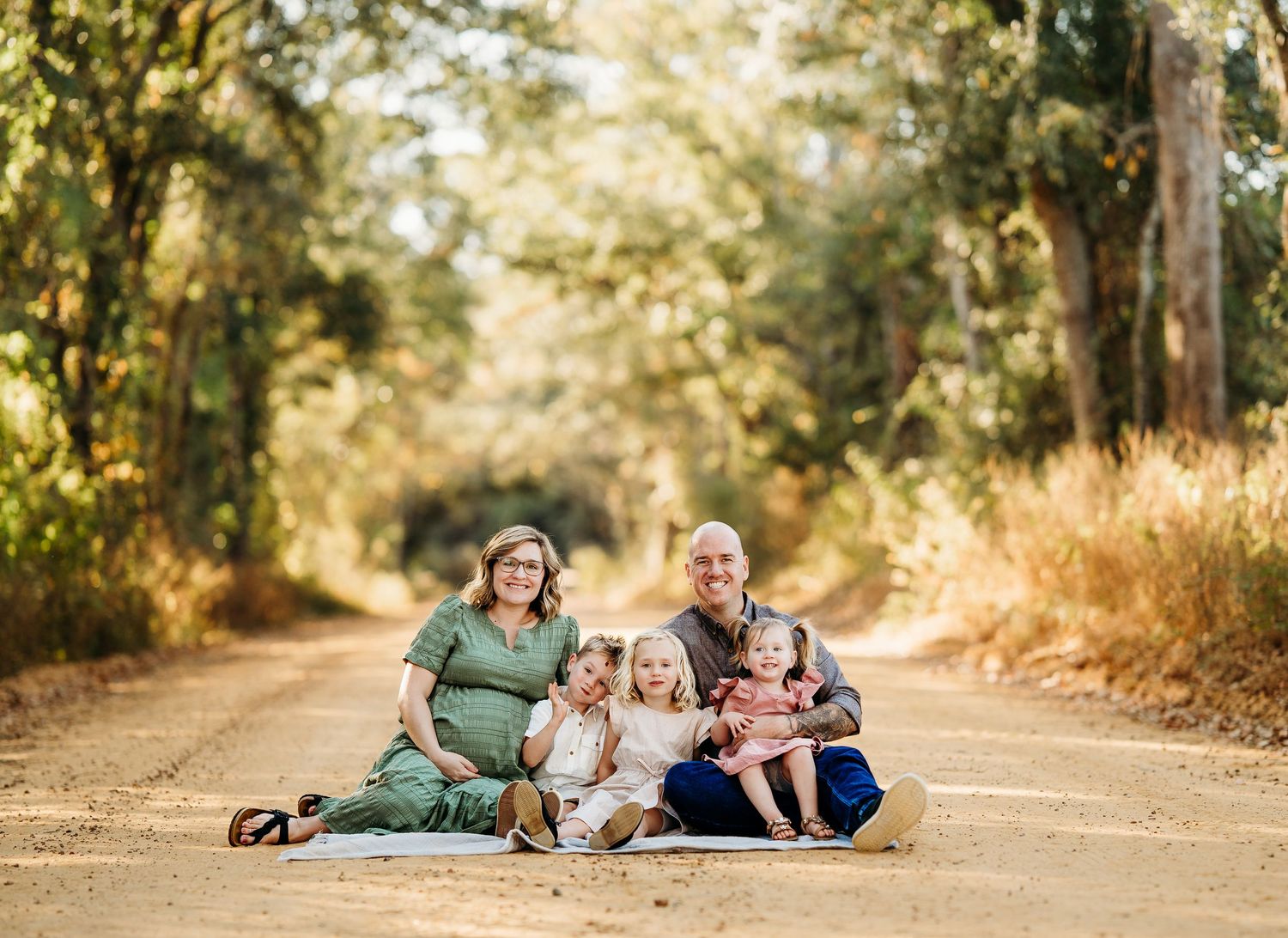 Happy family with young children sitting together on a scenic dirt road surrounded by trees.