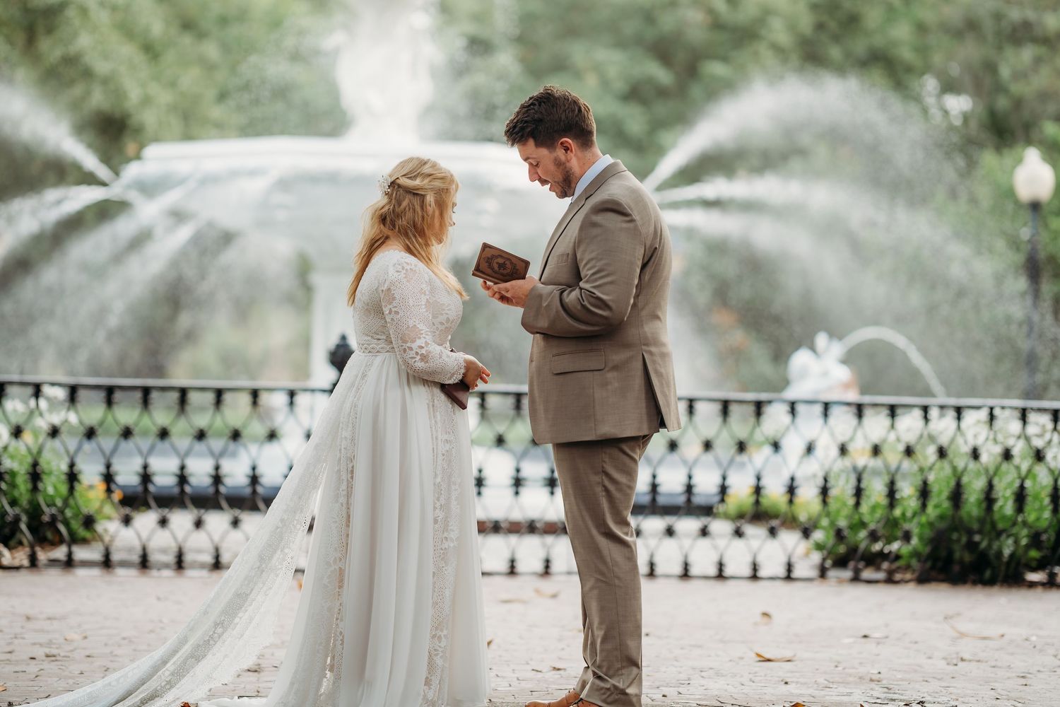 Bride and groom exchange vows in front of a fountain during an elegant outdoor park wedding.