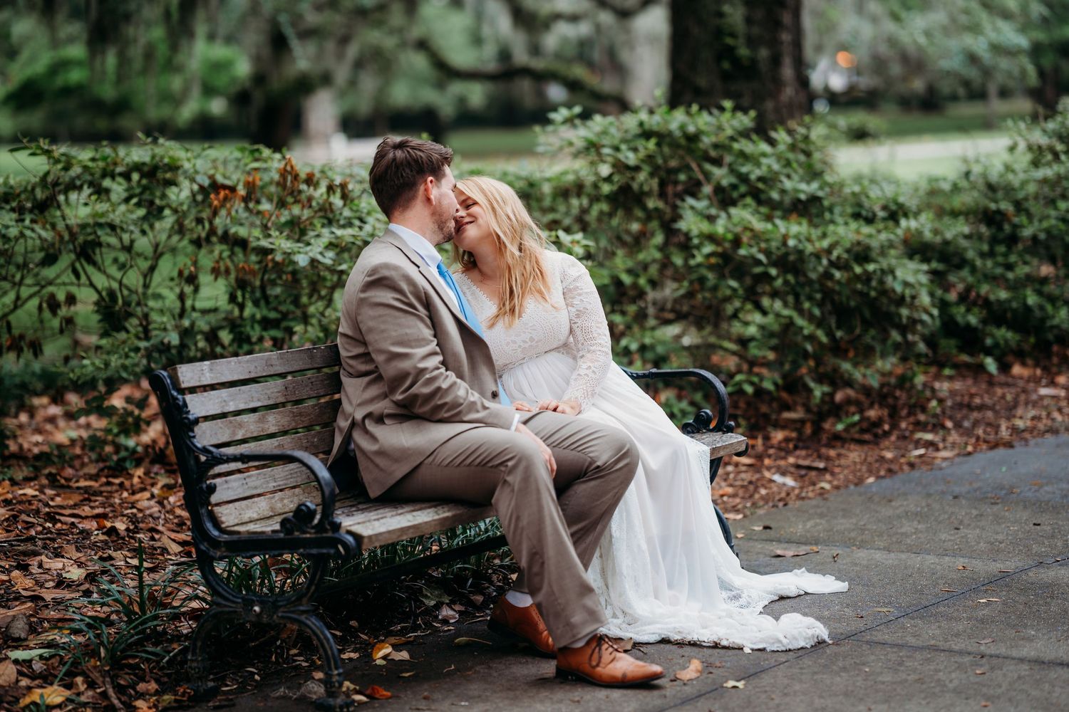 Romantic couple in wedding attire sharing an intimate moment on a park bench amid fall foliage.