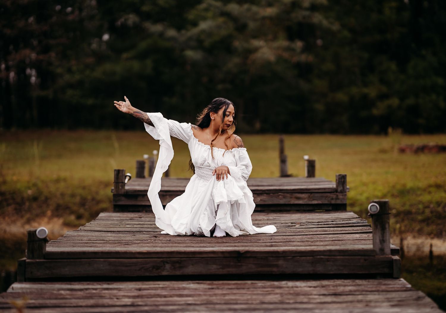 Two women in white dresses posing together on rustic wooden pier in nature.