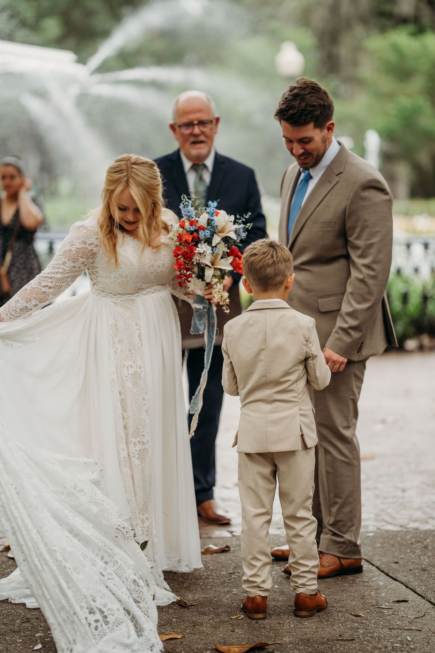 Bride, groom, and ring bearer sharing sweet moment at outdoor wedding ceremony.
