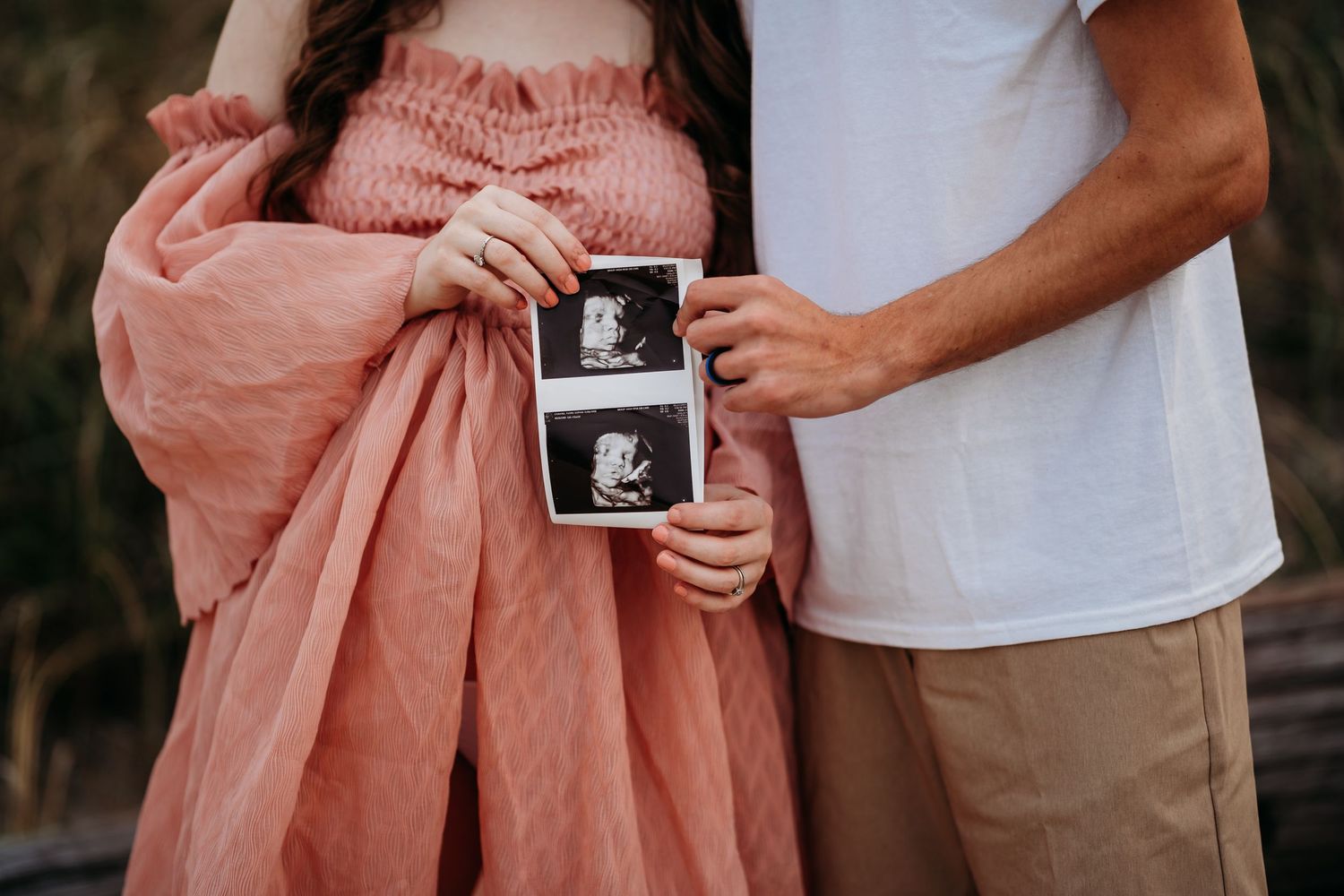Close-up of expecting couple holding ultrasound photos during outdoor maternity photo session.
