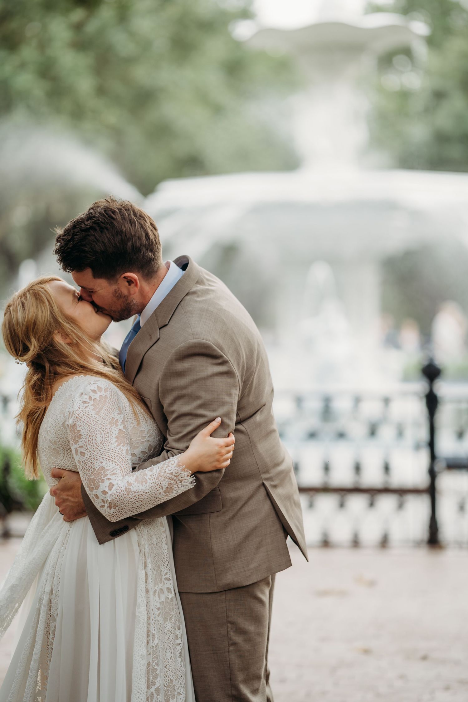 Bride and groom share their first kiss as newlyweds in front of a beautiful outdoor fountain.