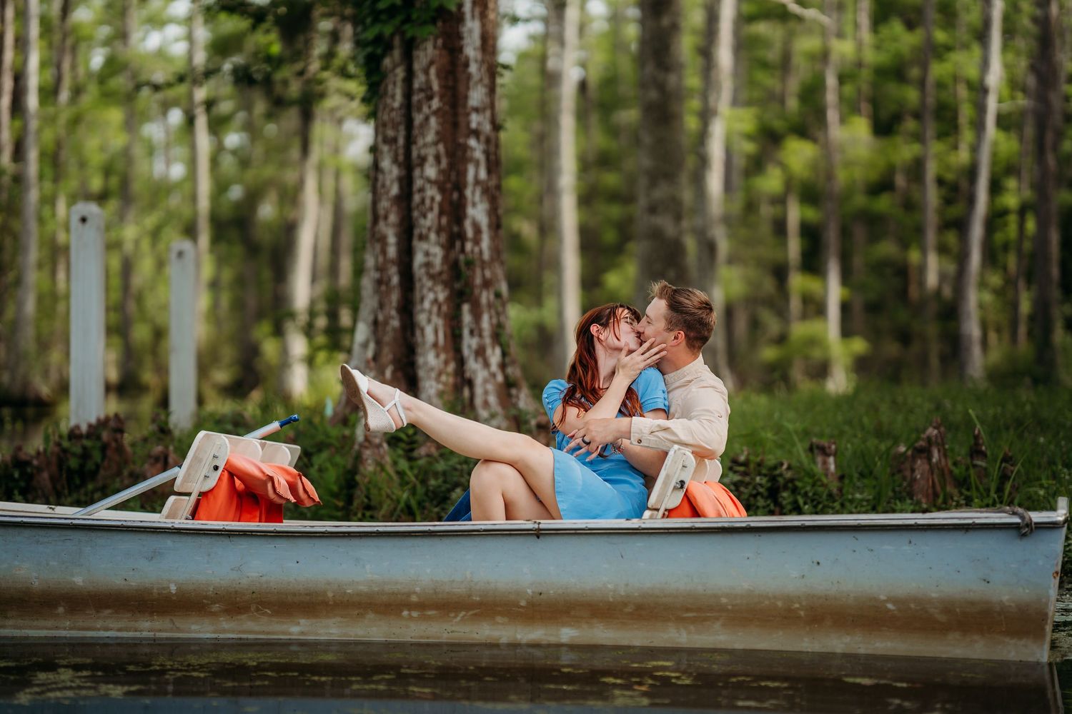 Romantic couple kissing in a canoe surrounded by lush green forest trees on a calm lake.