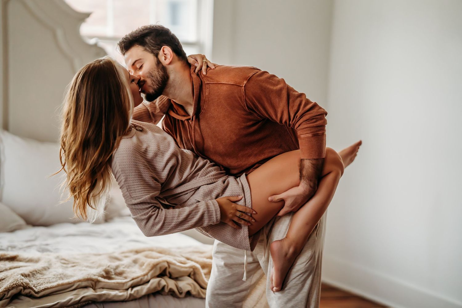 A couple shares a romantic dip near a bed, the man in a brown shirt holding her close.