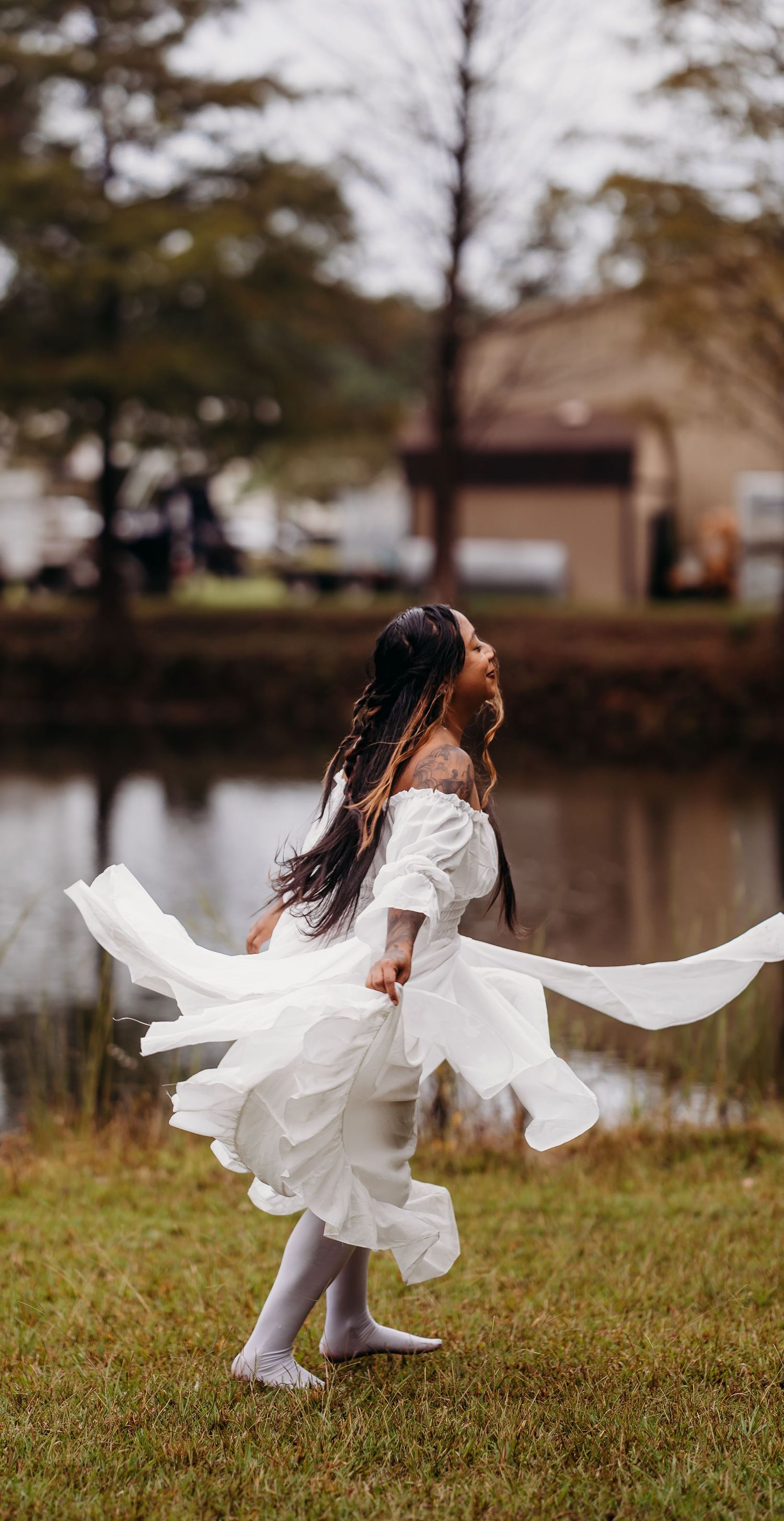 Woman twirling in flowing white dress near pond in autumn park.