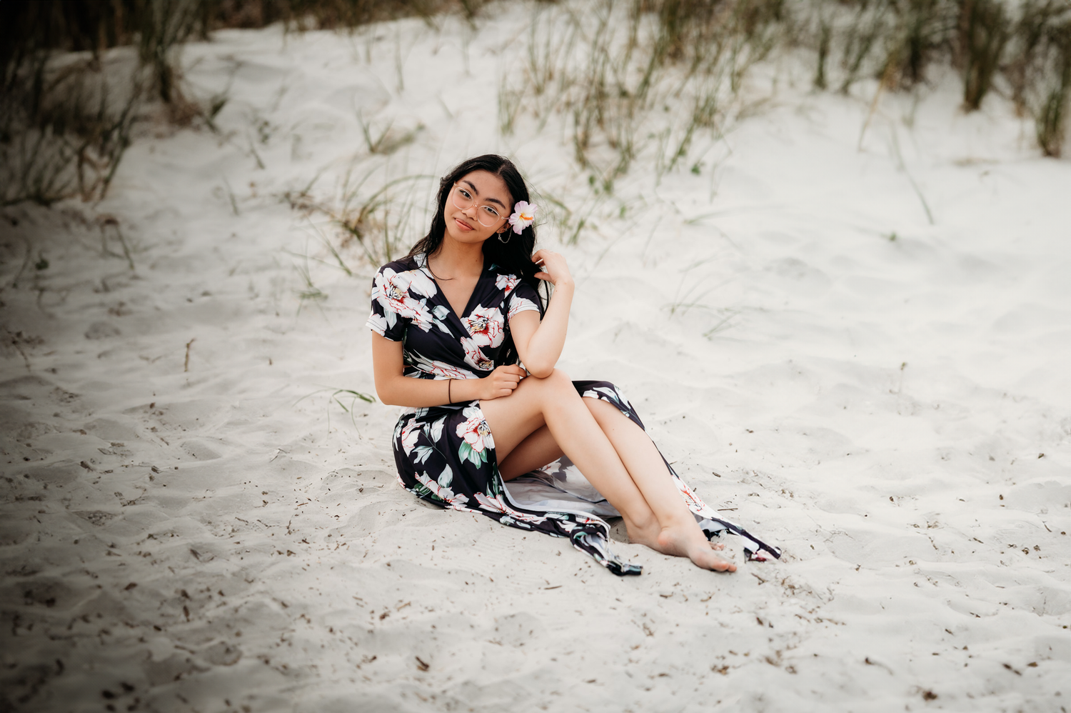 Woman in floral dress sitting on white sand beach dunes, posing gracefully for a portrait photo.