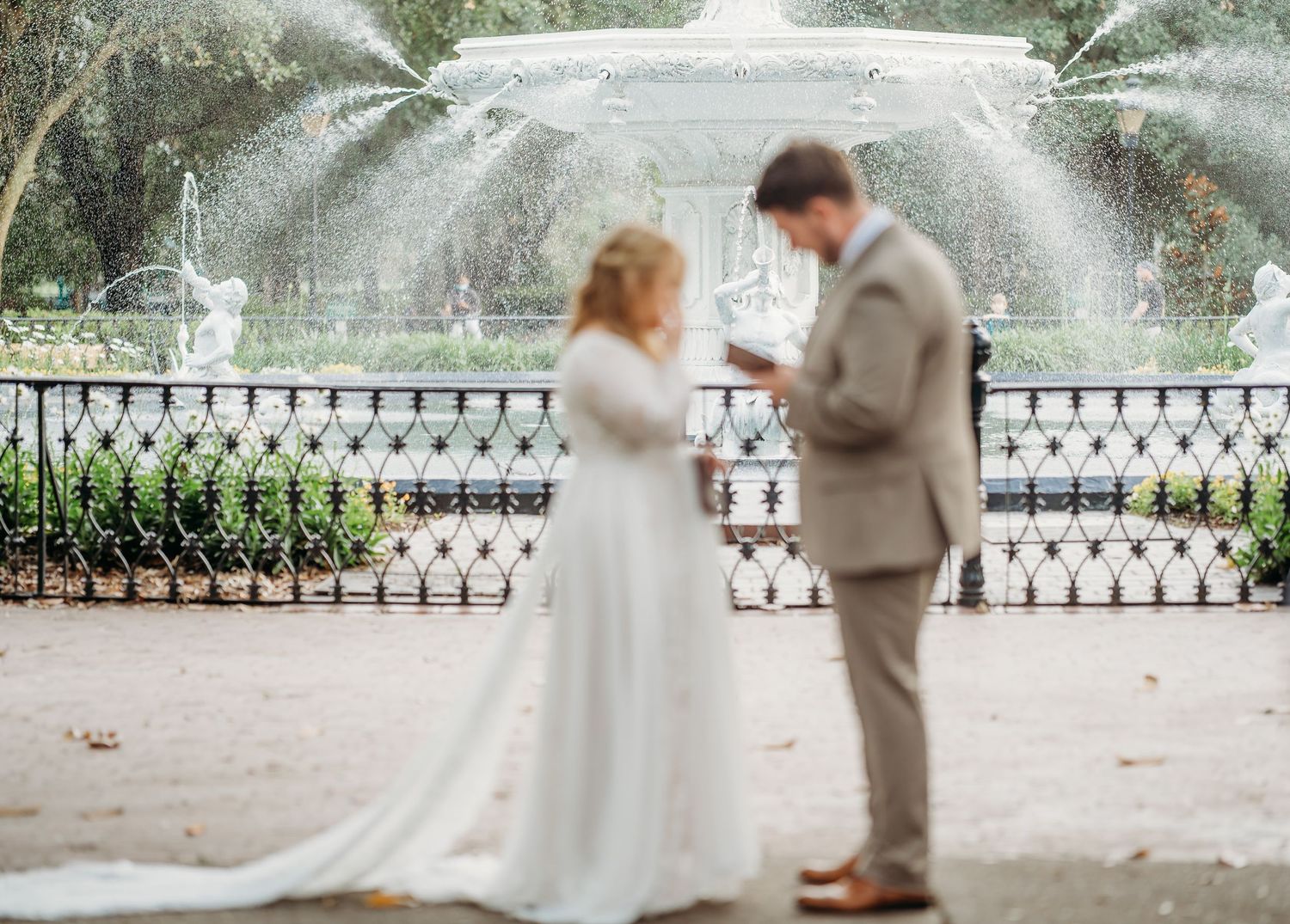 Bride and groom exchange vows in front of a grand fountain during an outdoor wedding ceremony.