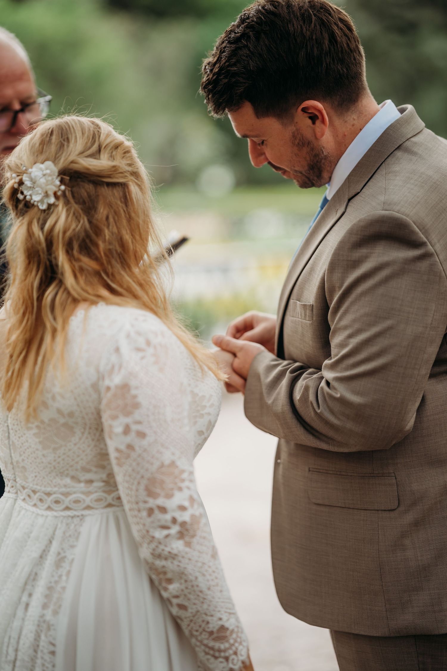 Groom carefully slides wedding ring onto bride's finger during emotional outdoor ceremony.
