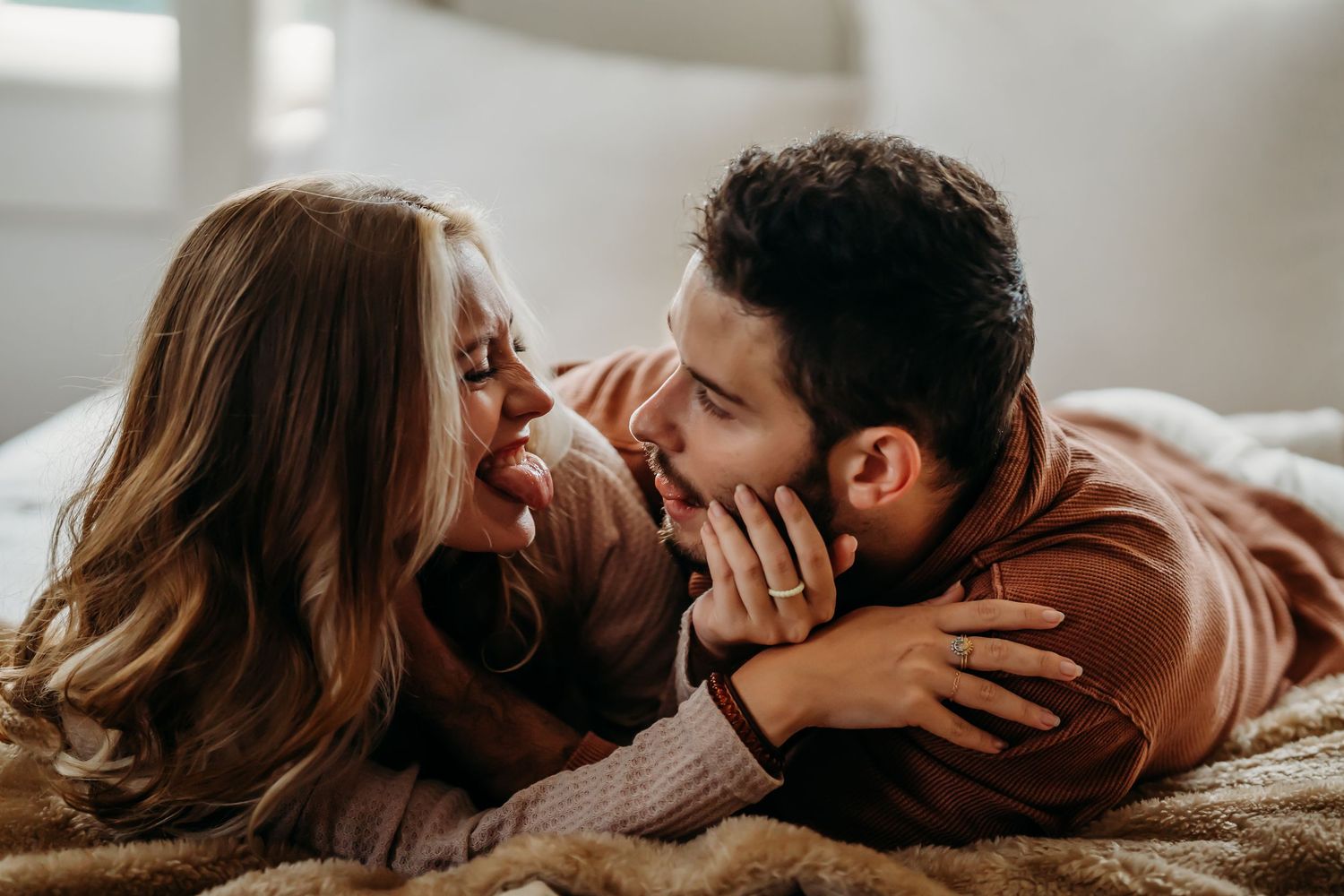 Joyful couple laughing and cuddling face-to-face while lying on a cozy fur blanket.