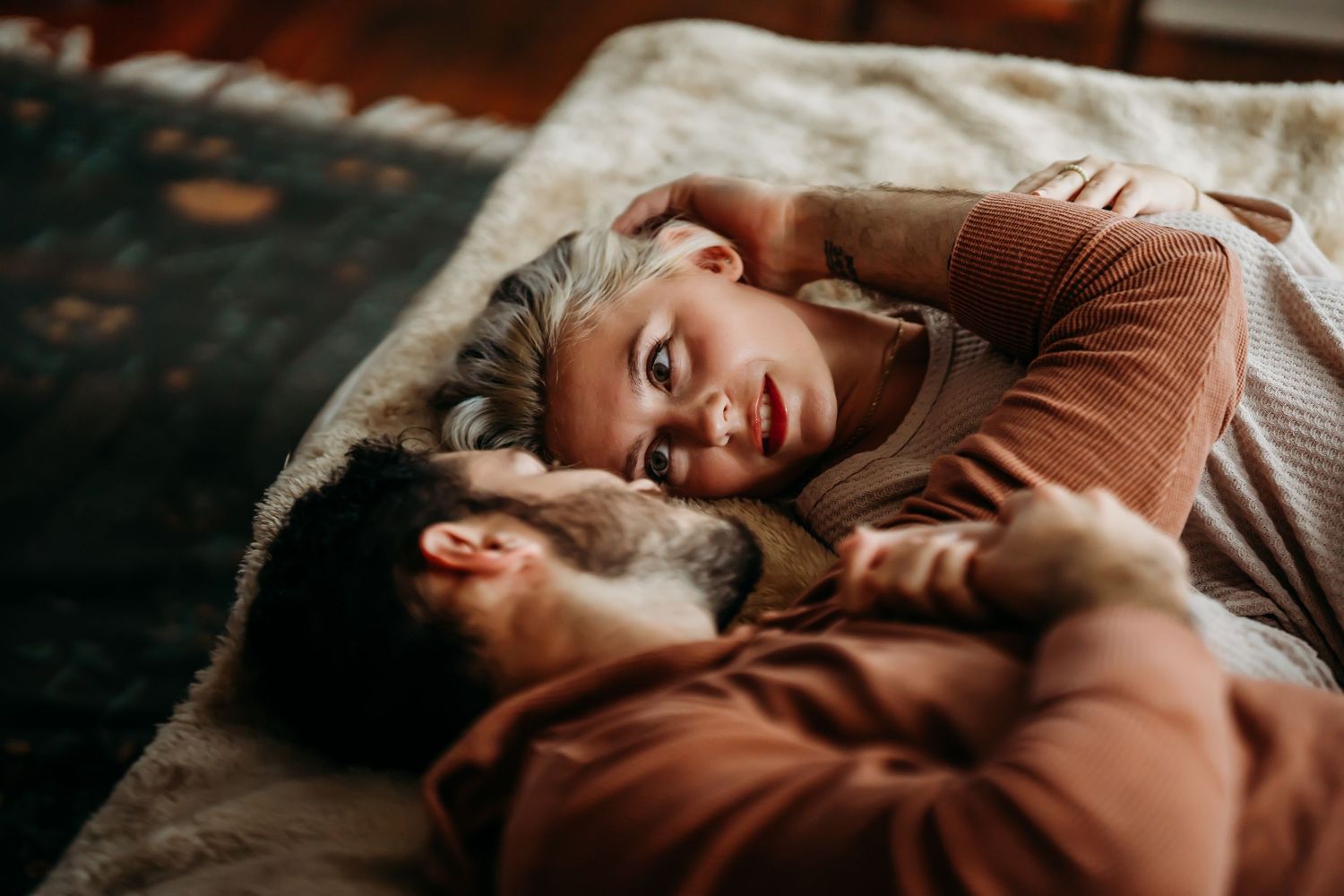 Romantic couple lying together on bed, woman with blonde hair gazing lovingly at partner.