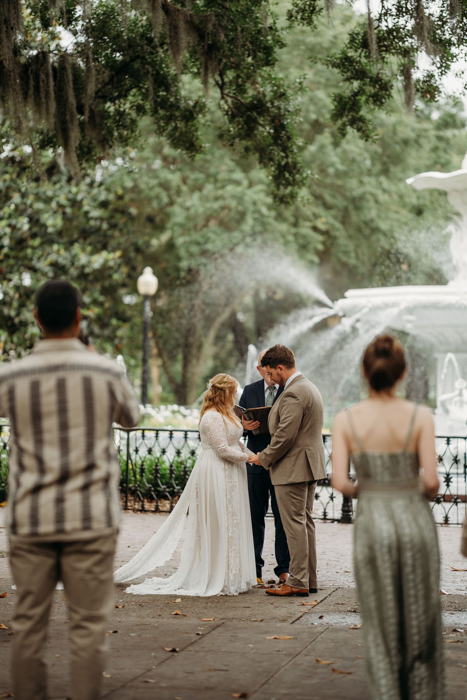 Bride and groom exchange vows before Forsyth Park fountain in Savannah with small group of guests watching.
