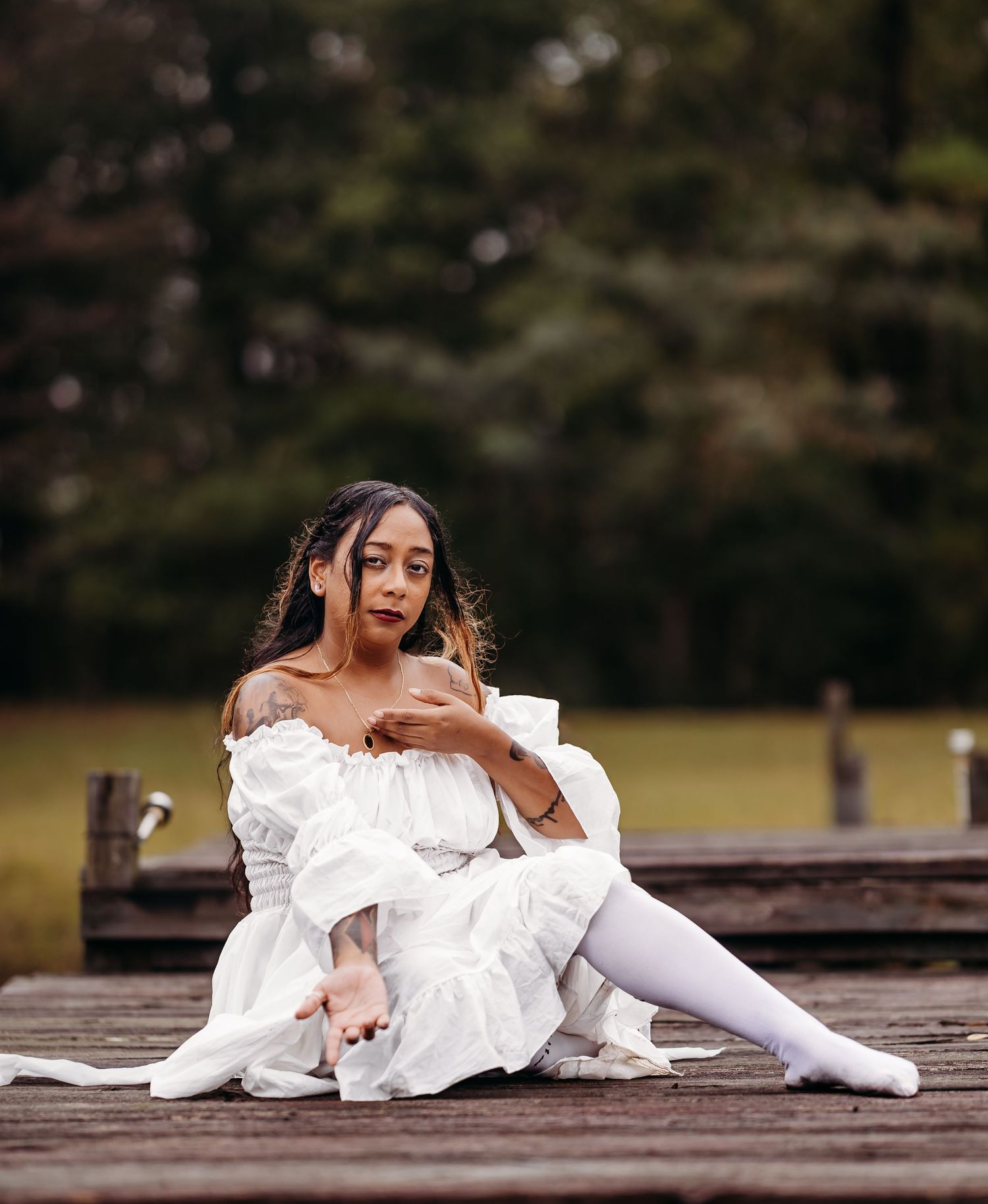 Woman in white ruffled off-shoulder dress and white stockings posing on wooden dock.