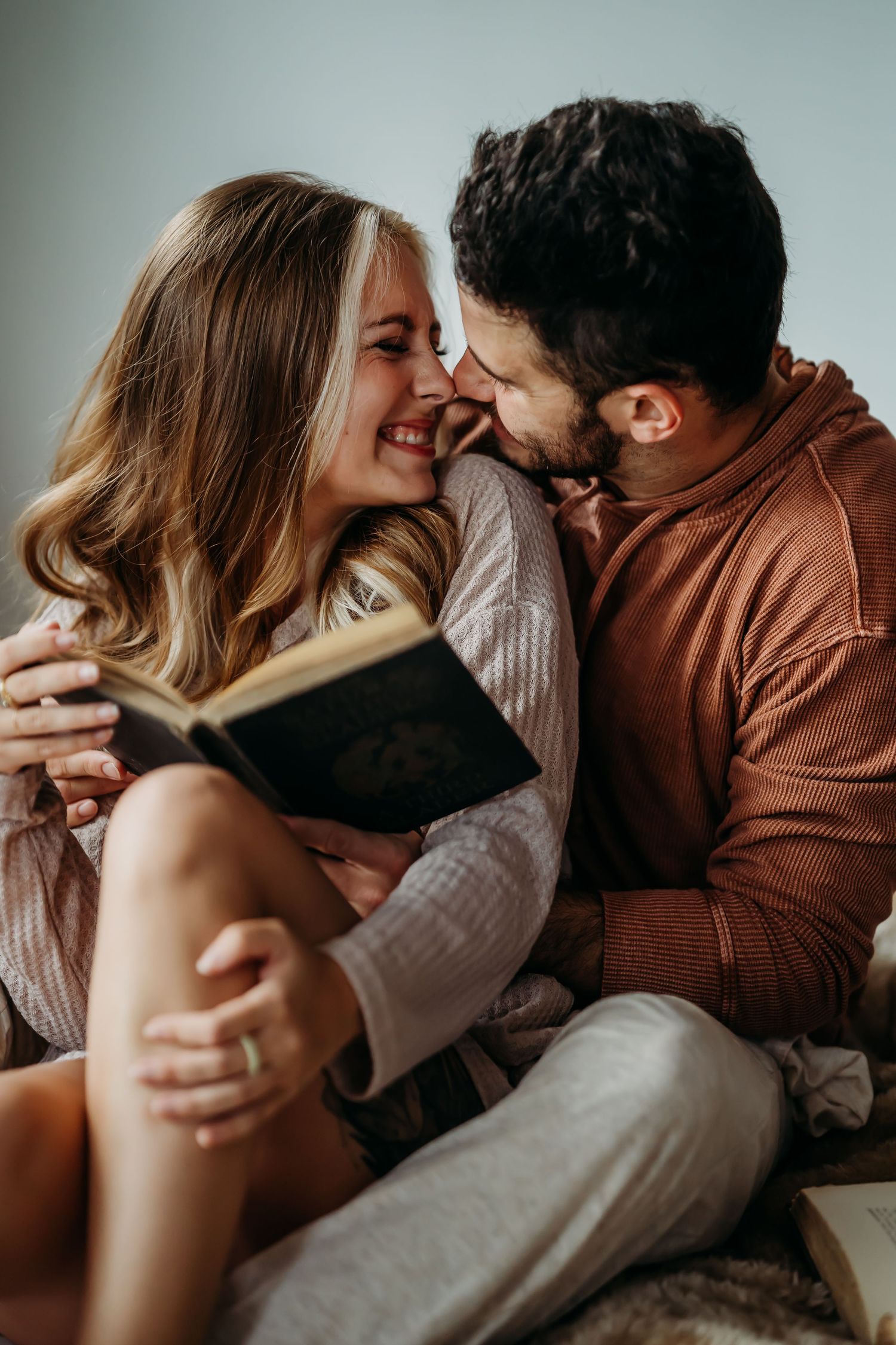 Happy couple smiling and touching noses while sharing book together in bed.