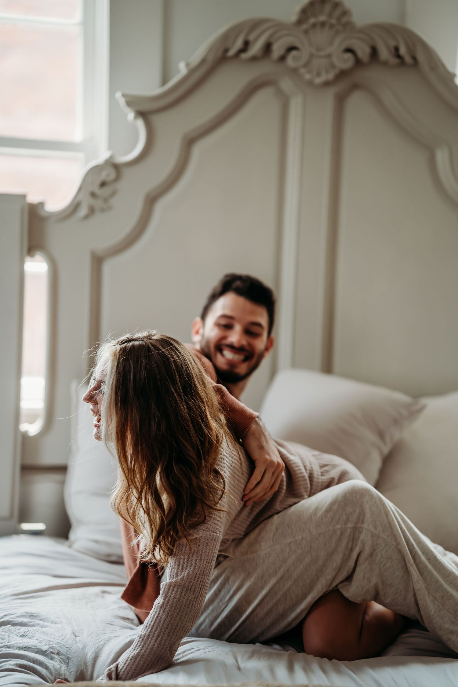 Smiling man gently touching womans hair while sitting together on elegant bed.