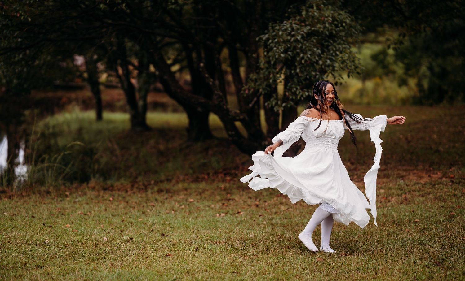 Woman in white dress dancing freely in green woodland clearing.