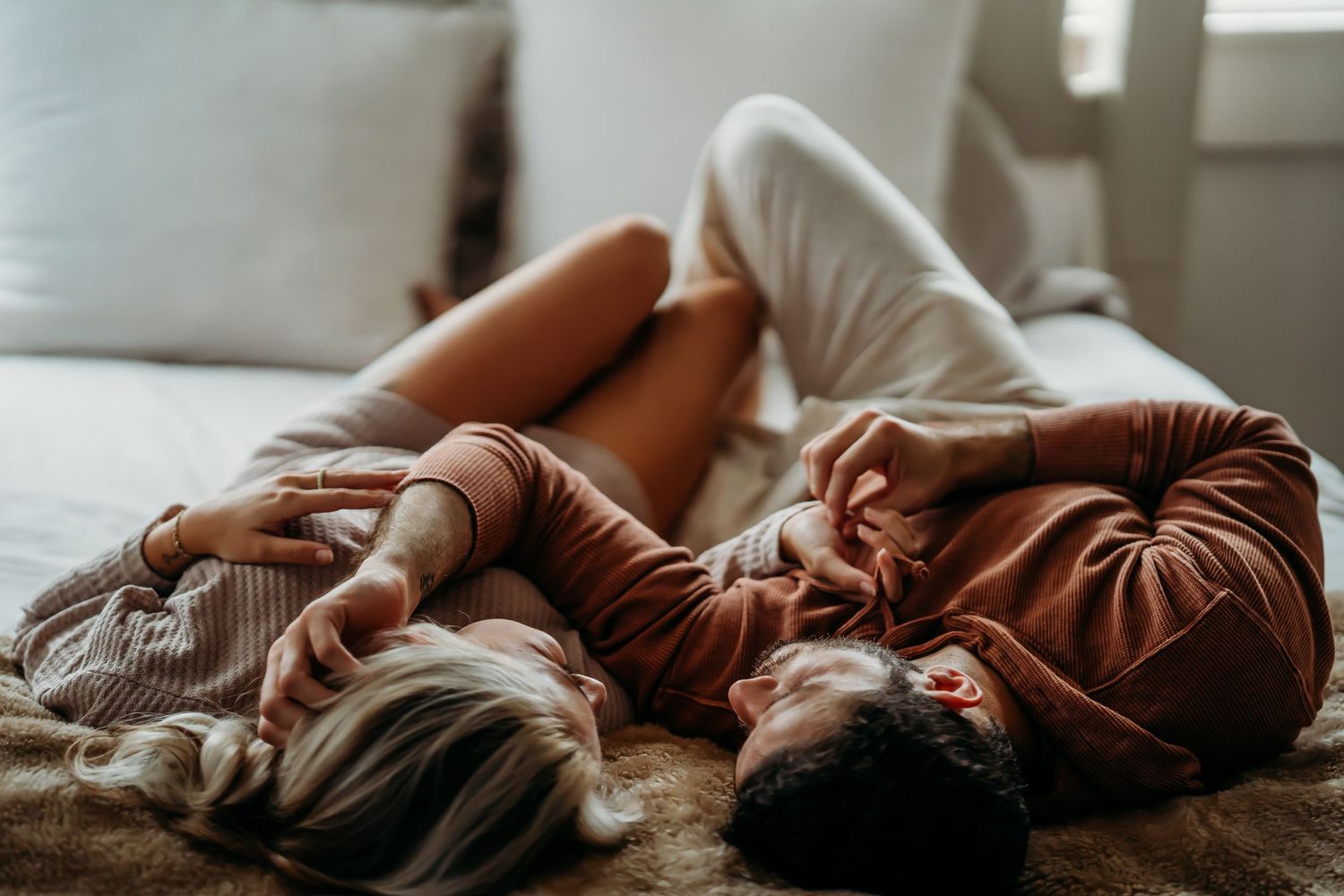 Couple lying on a bed together, holding hands and relaxing in a cozy bedroom.