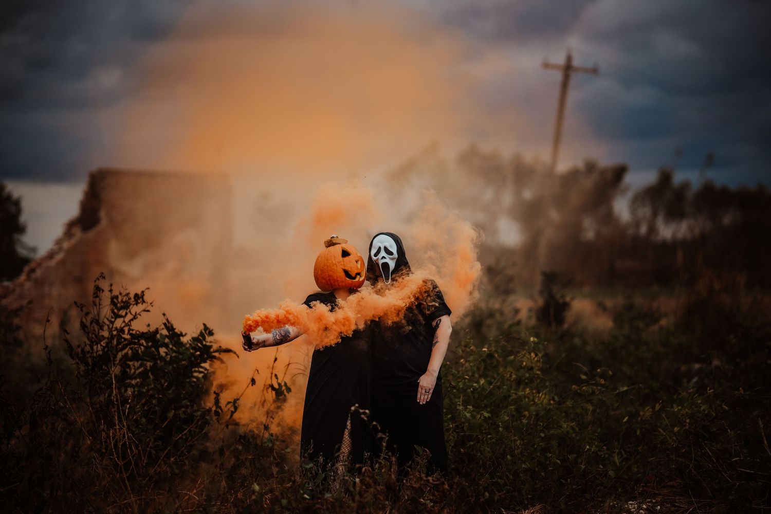 Two people in Halloween costumes with orange smoke bomb in dramatic outdoor scene.