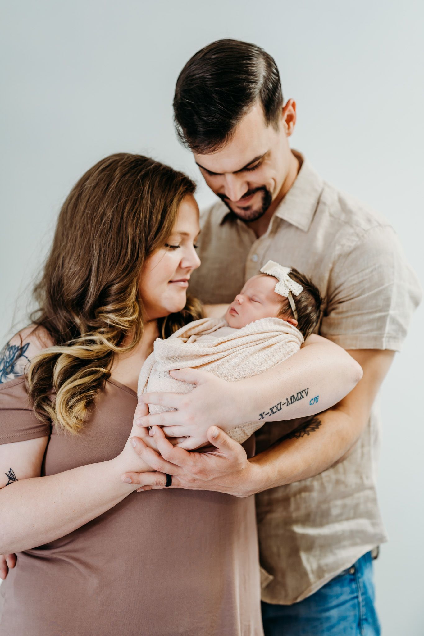 New parents lovingly cradle their swaddled newborn baby girl during a studio newborn photography session.