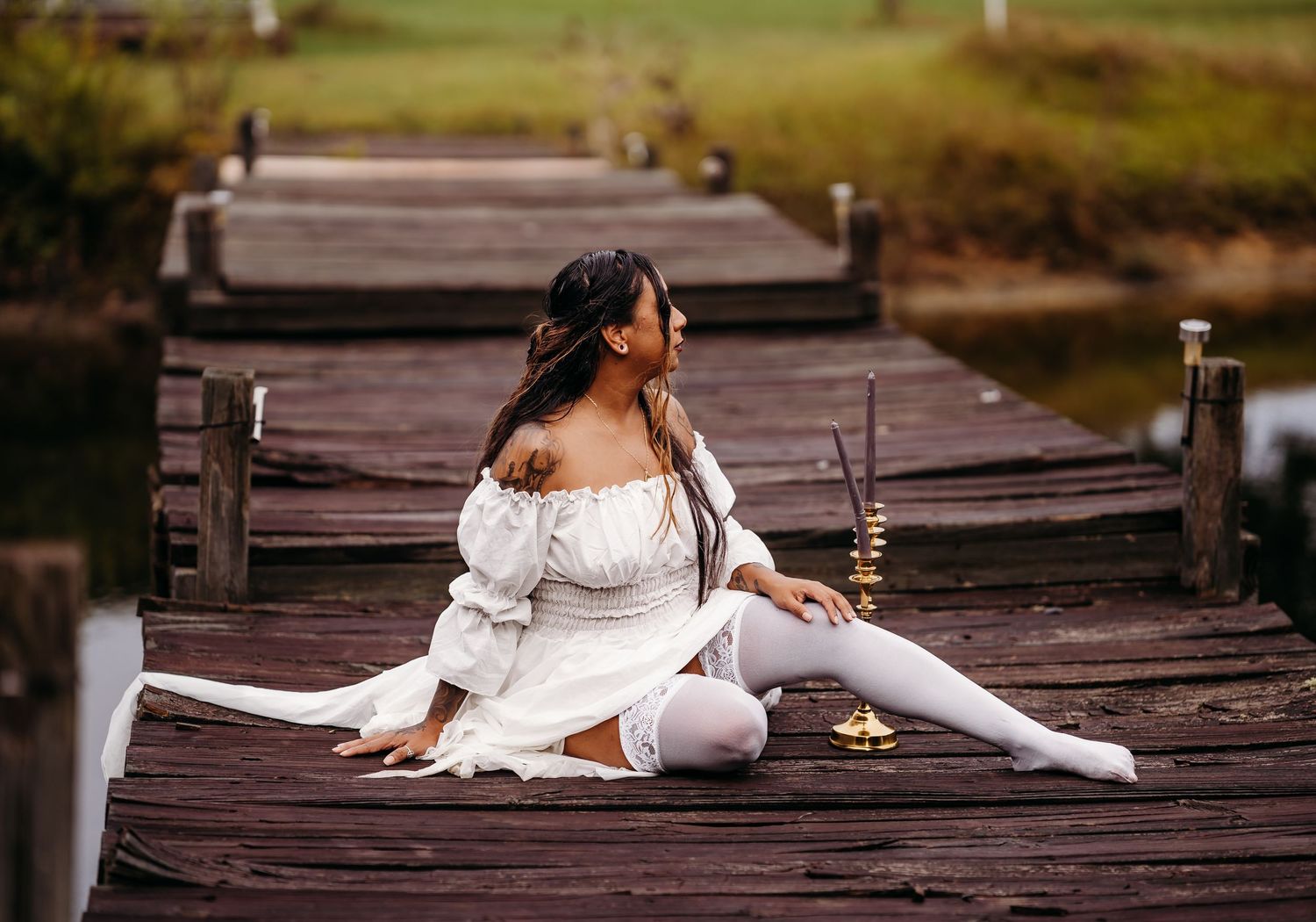 Woman in white dress and thigh-high stockings sits in splits pose on rustic wooden dock.
