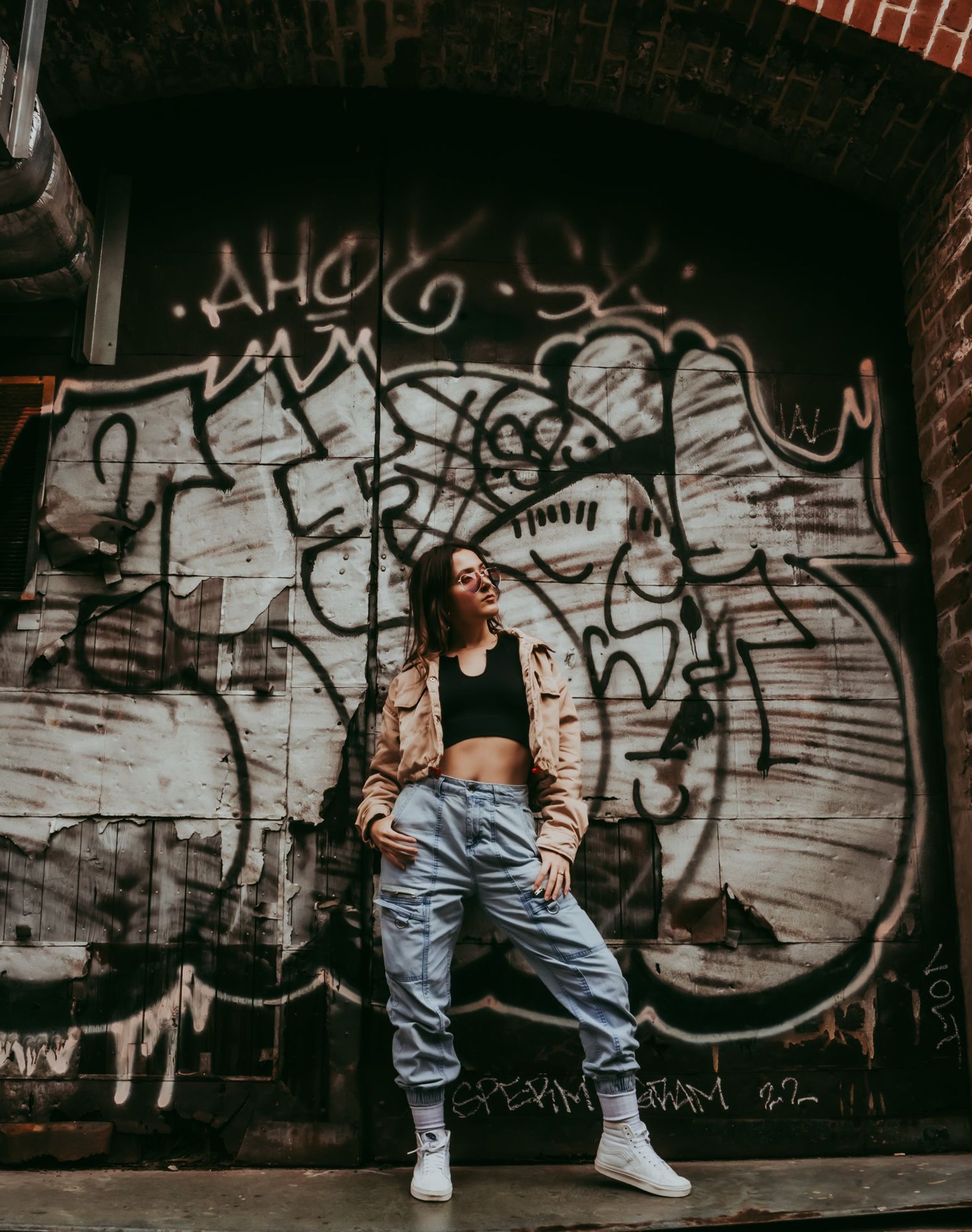 Woman in casual streetwear posing confidently in front of colorful urban graffiti wall.