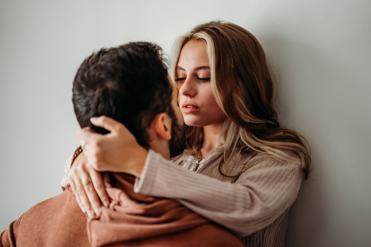 Tender couple embracing closely against white wall in intimate moment.