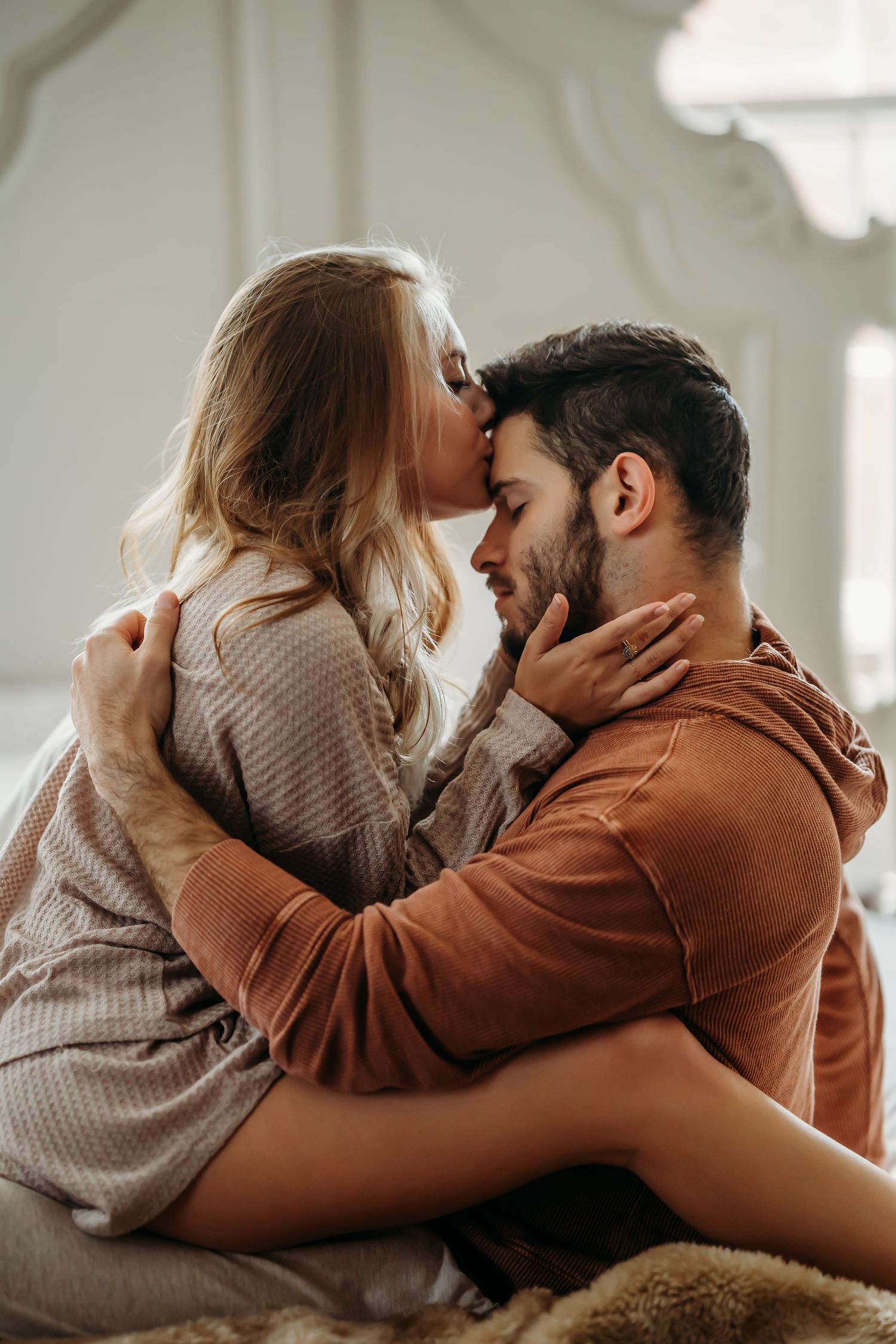 Couple embracing and kissing on a bed, woman cradling mans face tenderly indoors.
