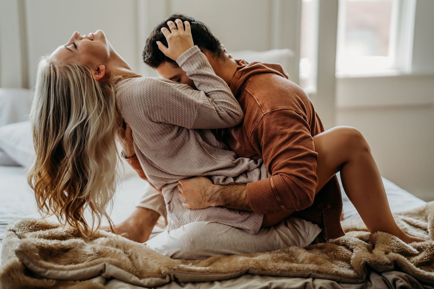 Passionate couple embracing and kissing on bed with cozy fur blanket in bright room.