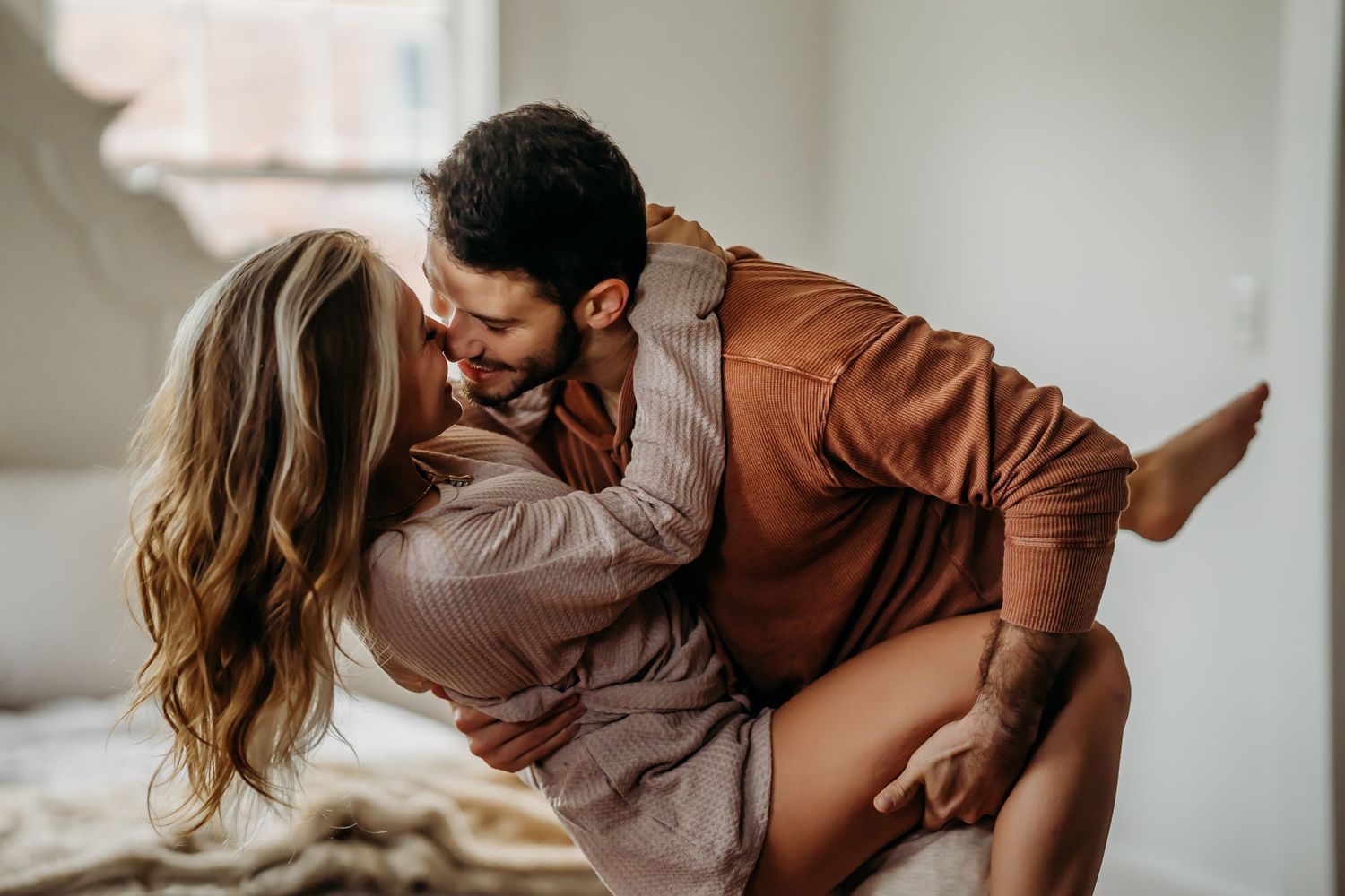 Joyful couple laughing and embracing each other in bright cozy bedroom.