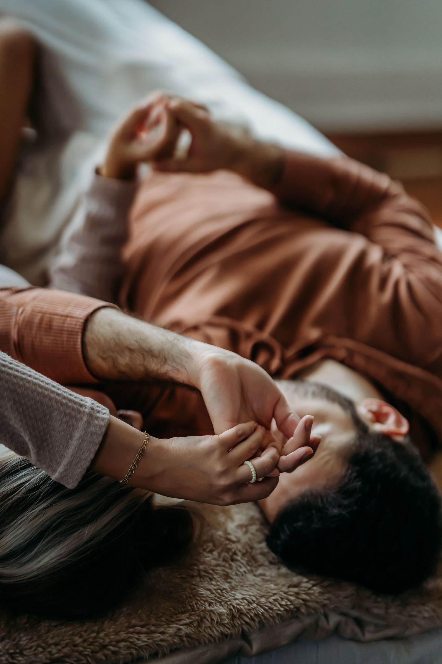 Close-up of a couple holding hands while lying on a cozy fur blanket together.
