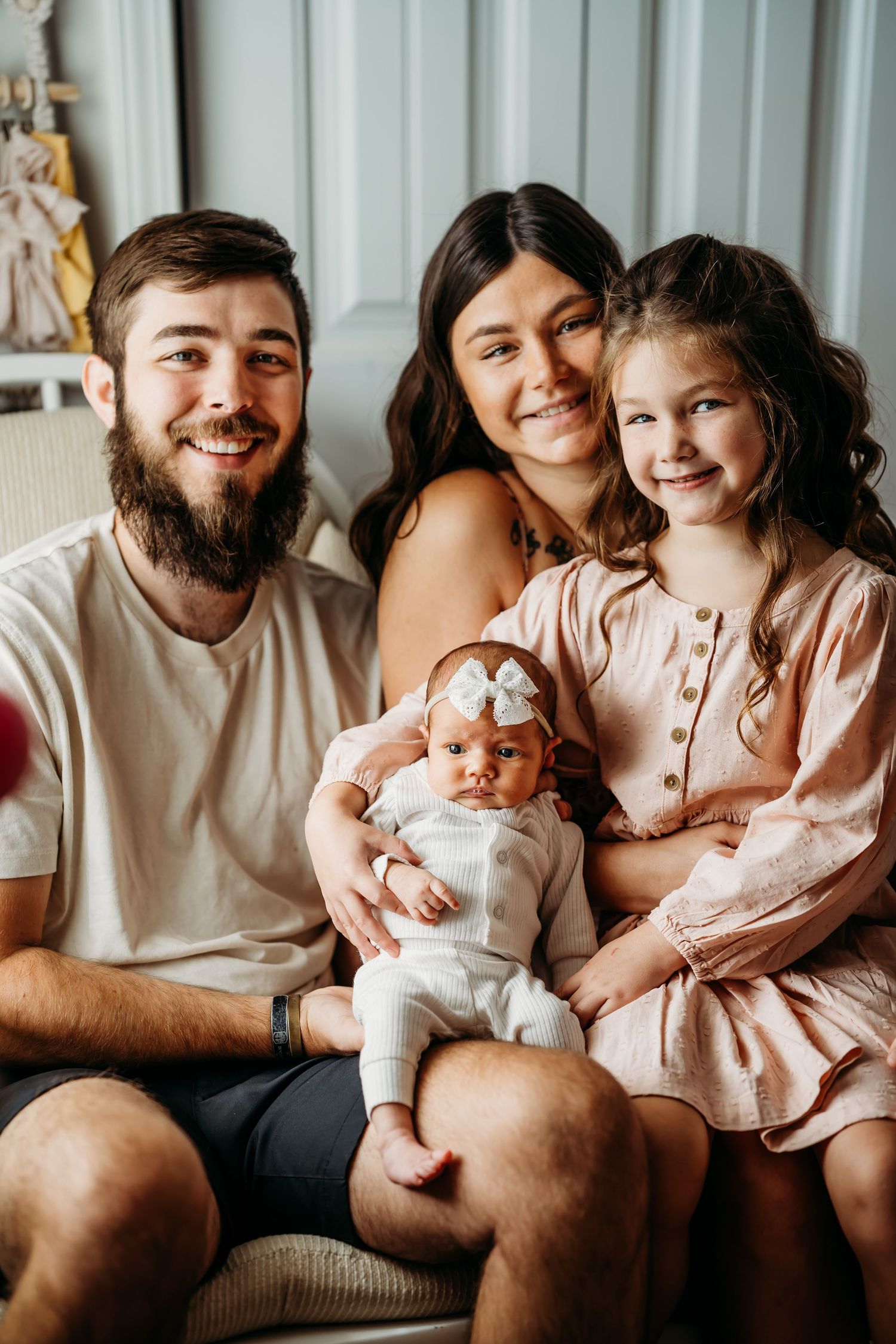 Happy family of four with newborn baby and toddler girl posing for indoor portrait photo session.