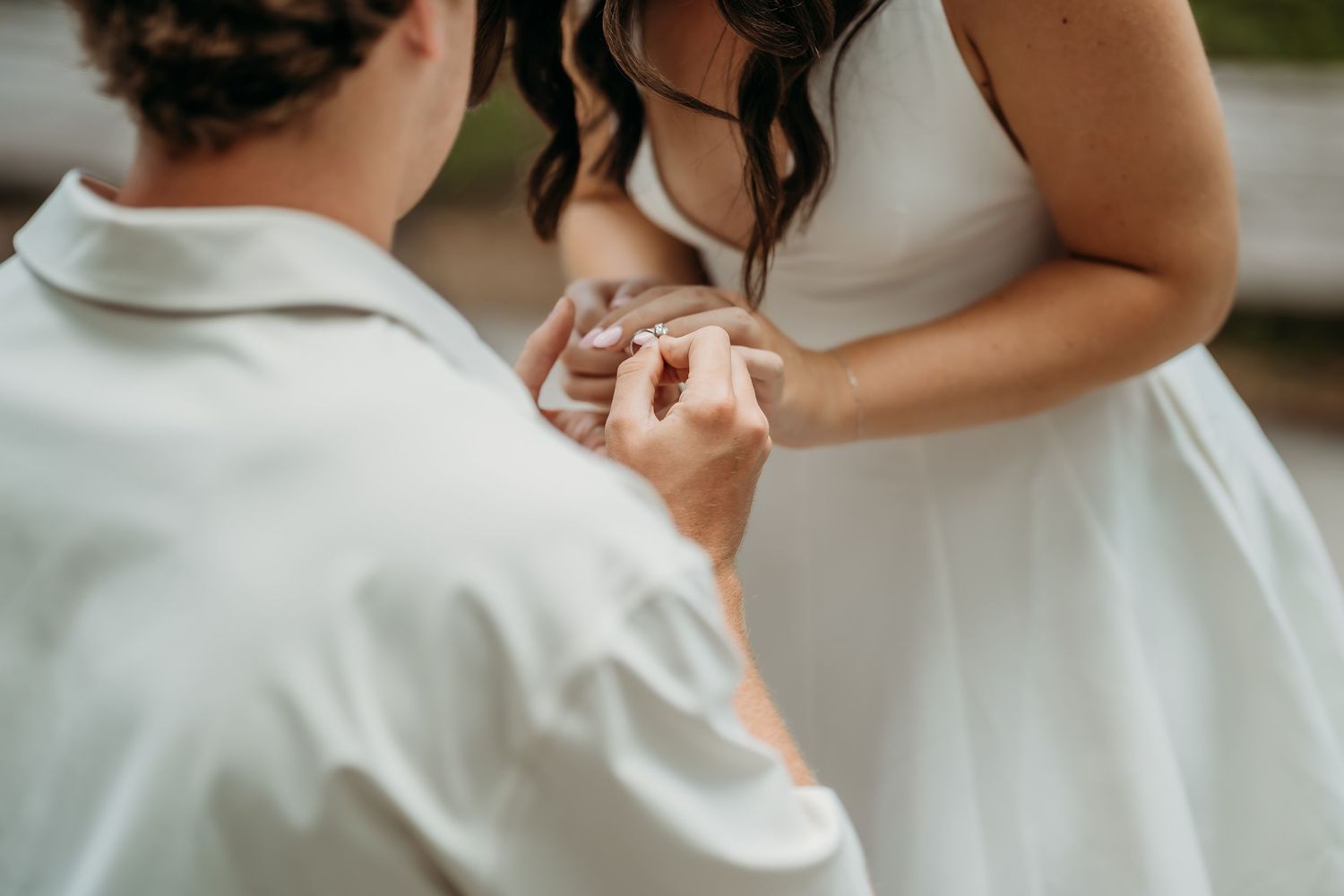 Groom placing a wedding ring on the brides hand during an intimate outdoor ring exchange ceremony.