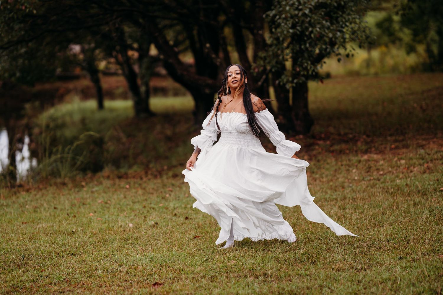 Joyful woman in white ruffled dress spinning freely on lush green lawn near trees.