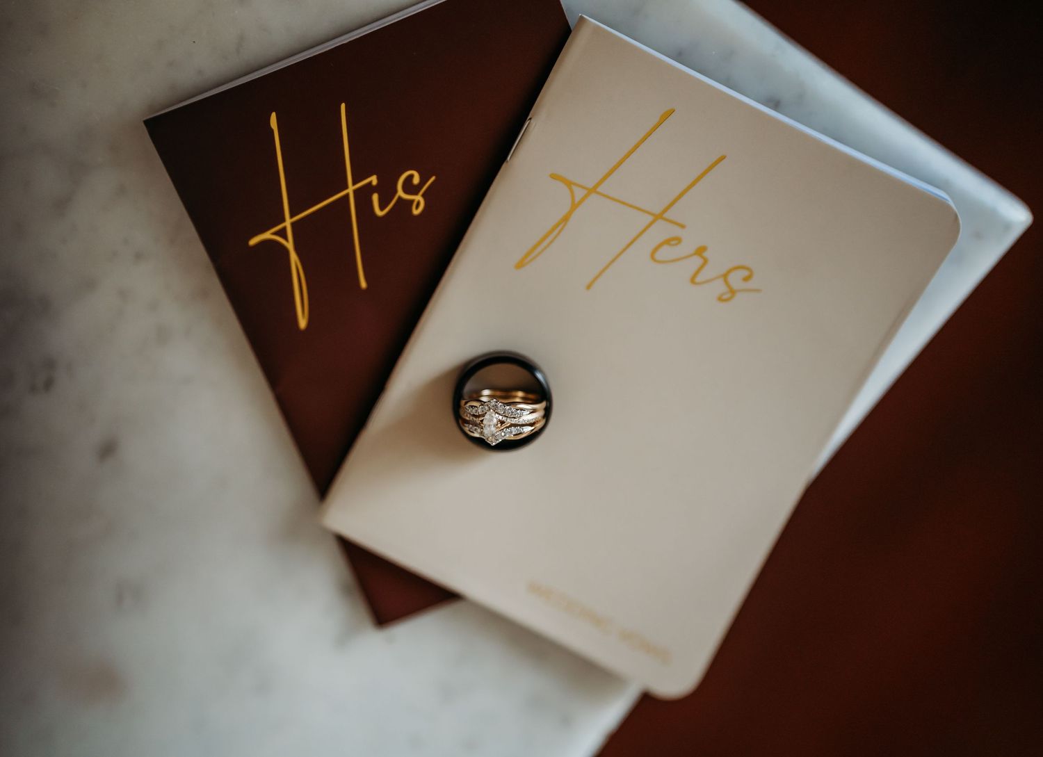 His and Hers wedding vow books with interlocked gold and silver wedding rings resting on top.