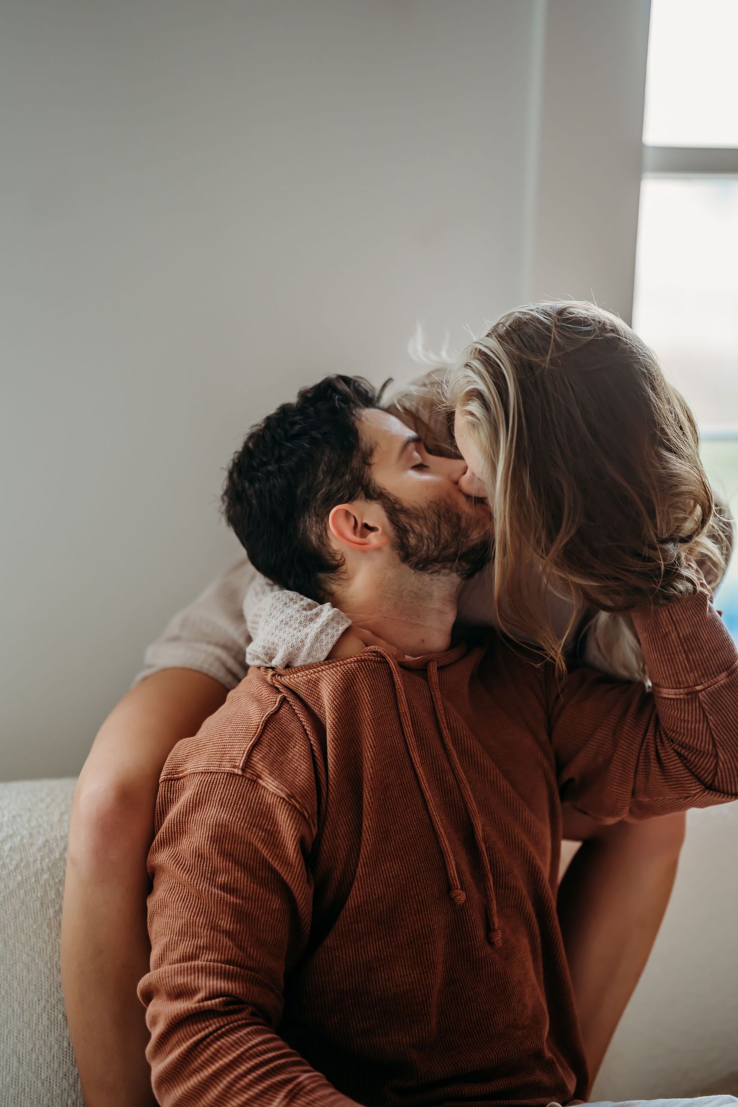 Couple sharing a tender kiss while sitting together in a cozy bedroom.