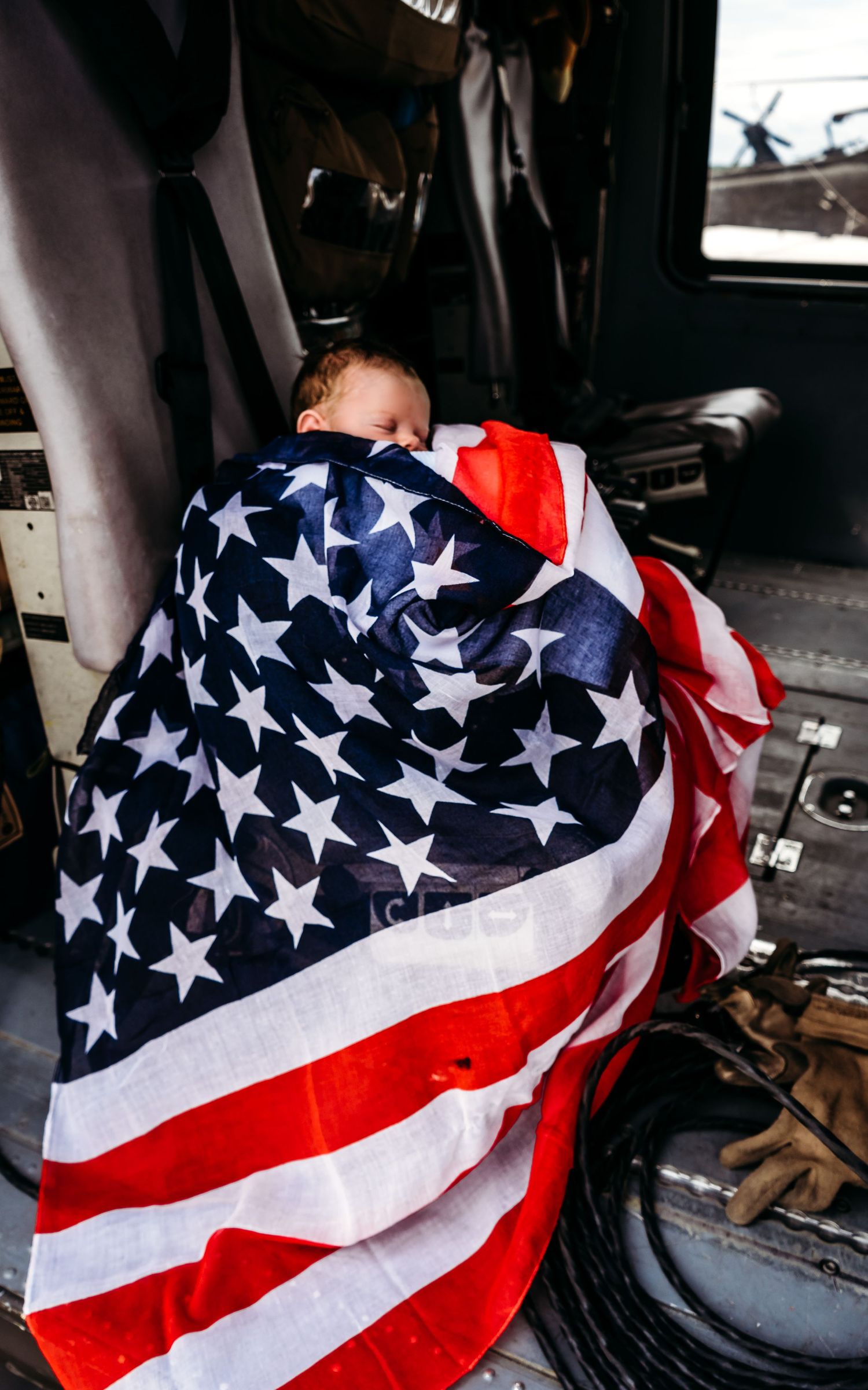 Newborn baby wrapped in an American flag inside a military vehicle cockpit.