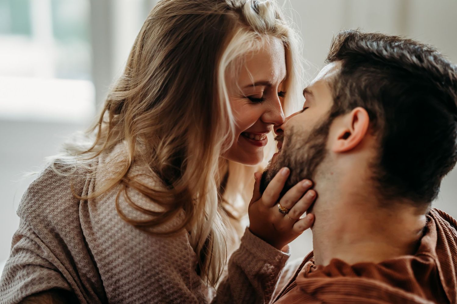 Playful couple laughing and almost kissing in bright natural light indoors.