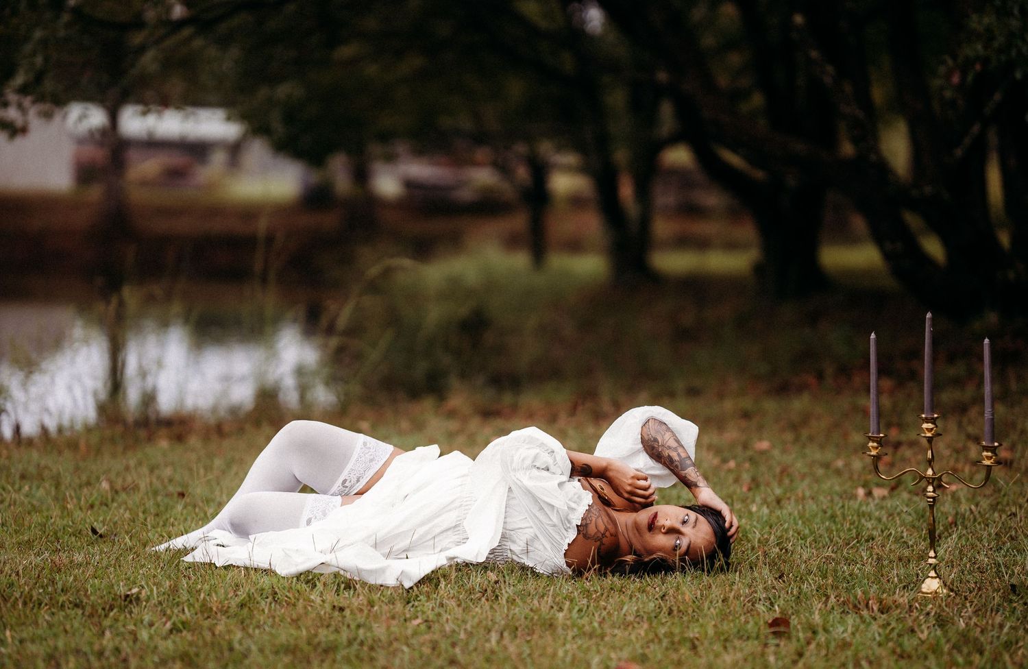 Woman in white dress lying on grass near pond with candelabra.