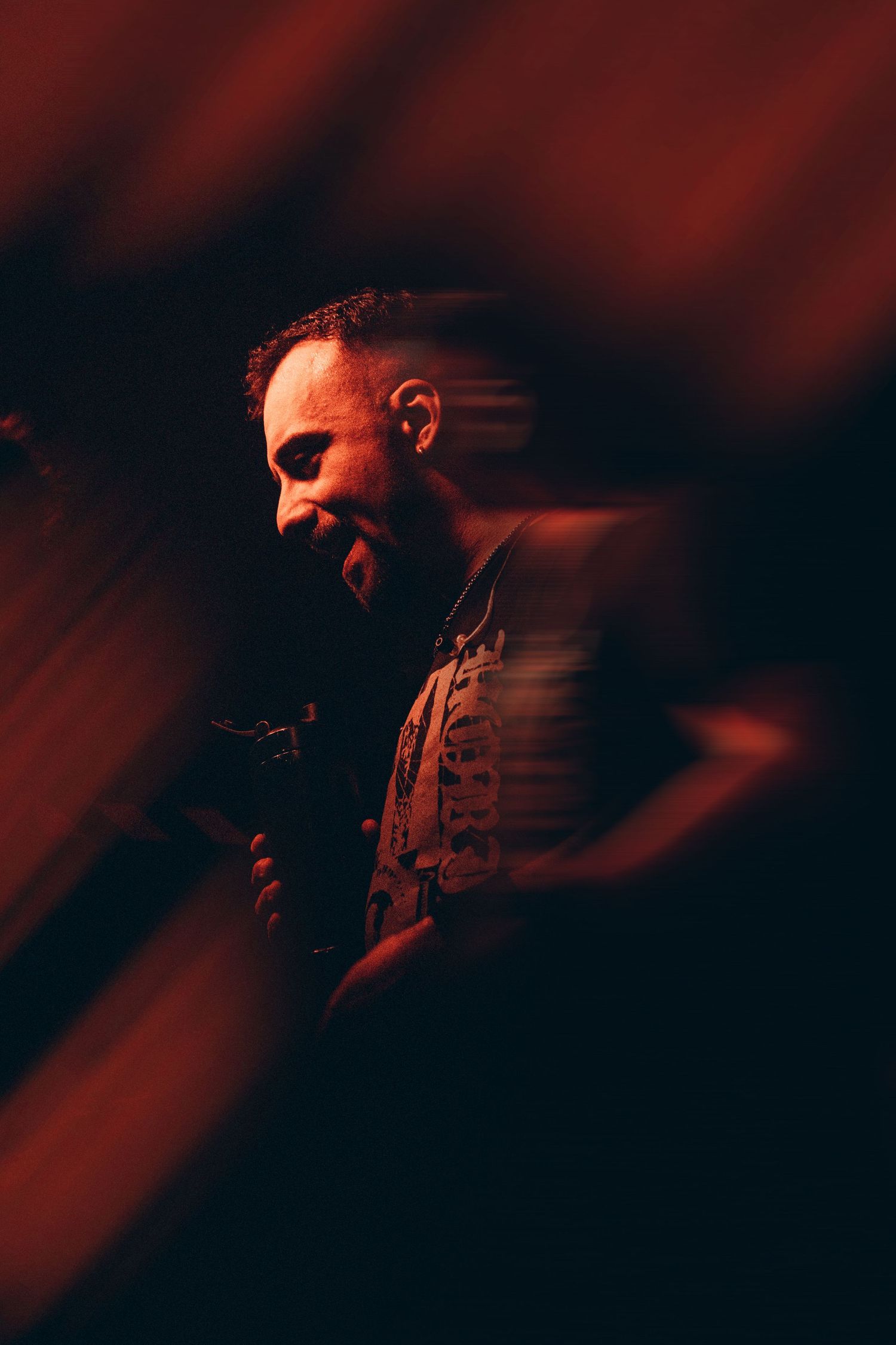 Male performer smiling under dramatic red lighting at a live music venue.