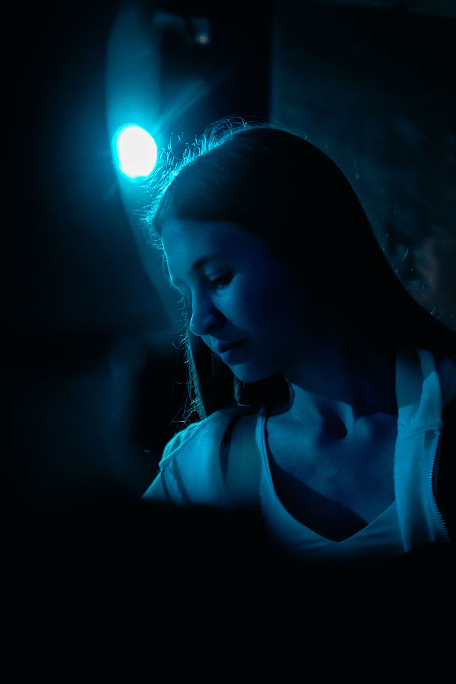 Young woman with long hair lit by blue stage light at a live performance.